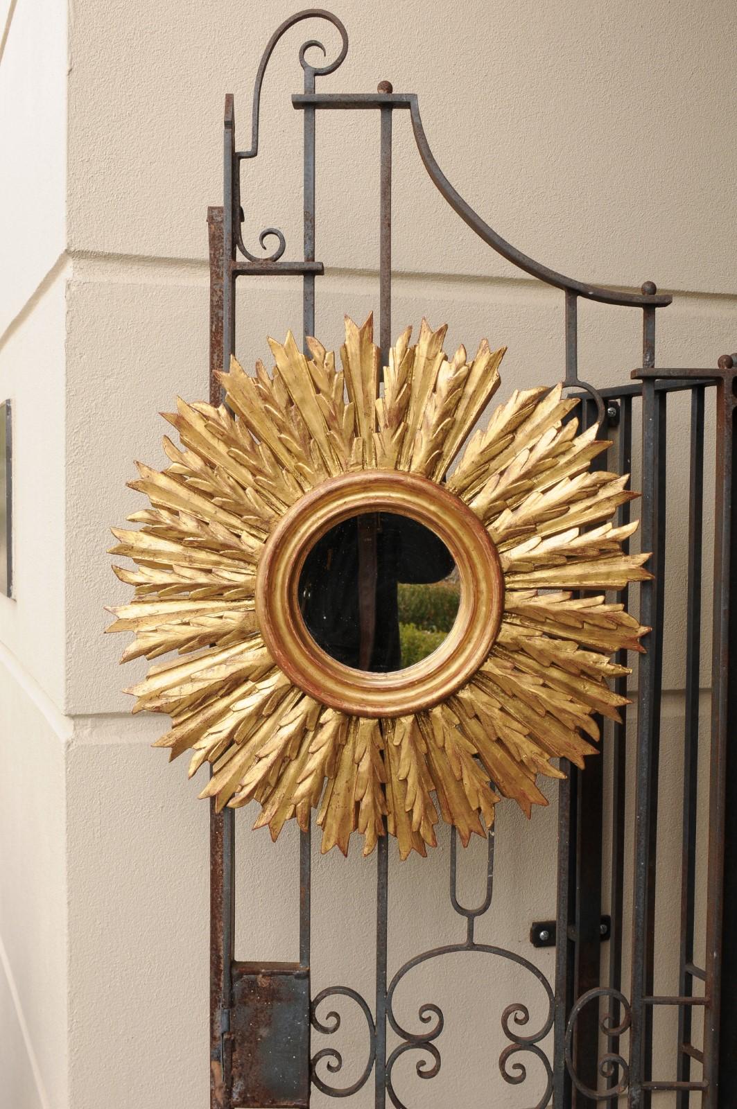 A French vintage carved giltwood sunburst mirror from the mid-20th century, with radiating sunrays. Born in France during the second quarter of the 20th century, this French giltwood sunburst mirror features a central mirror plate presenting slight