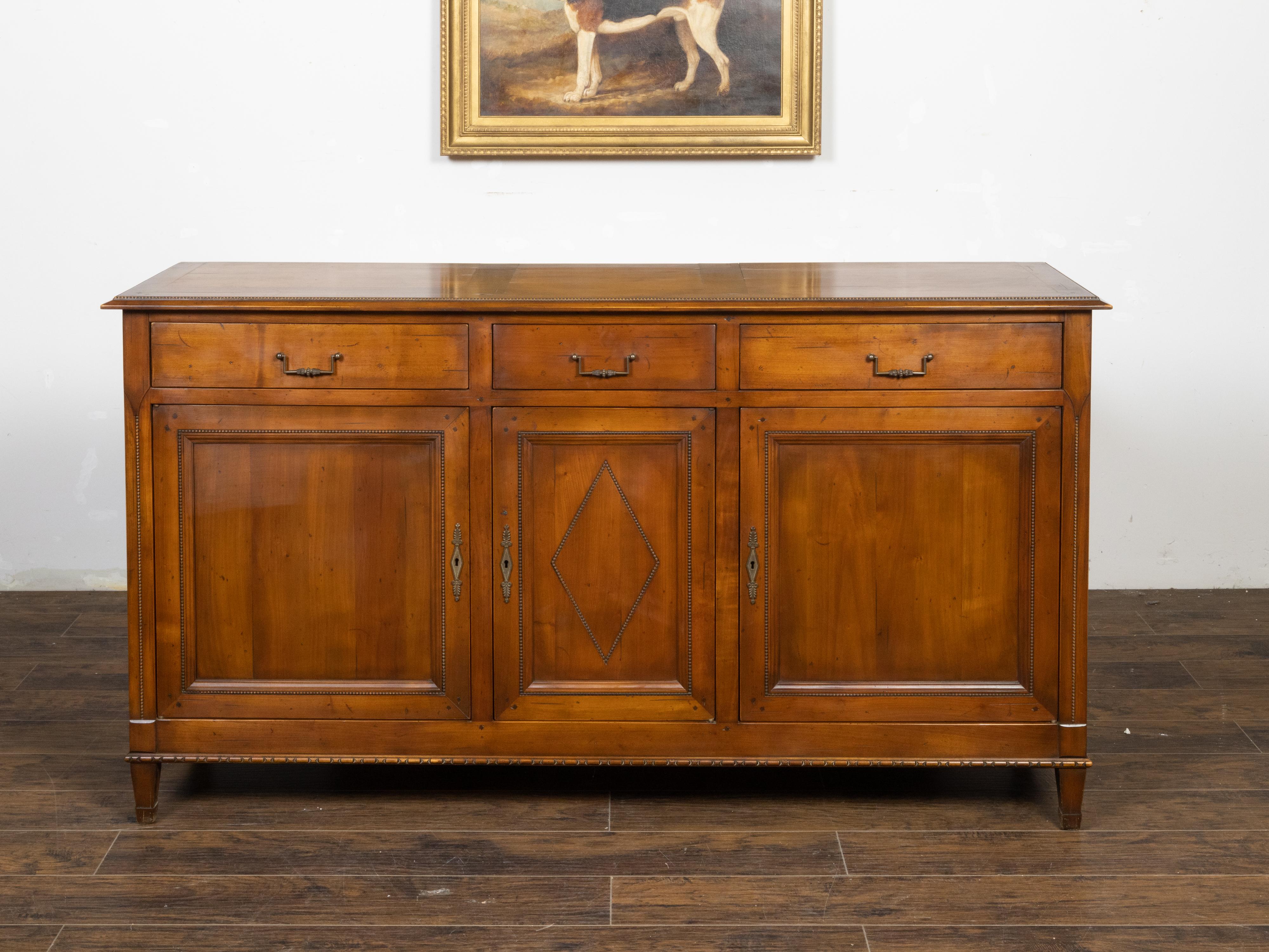 A French walnut enfilade from the mid-20th century with three drawers over three doors, carved beads and diamond motif. Created in France during the second quarter of the 20th century, this walnut enfilade features a rectangular top with three
