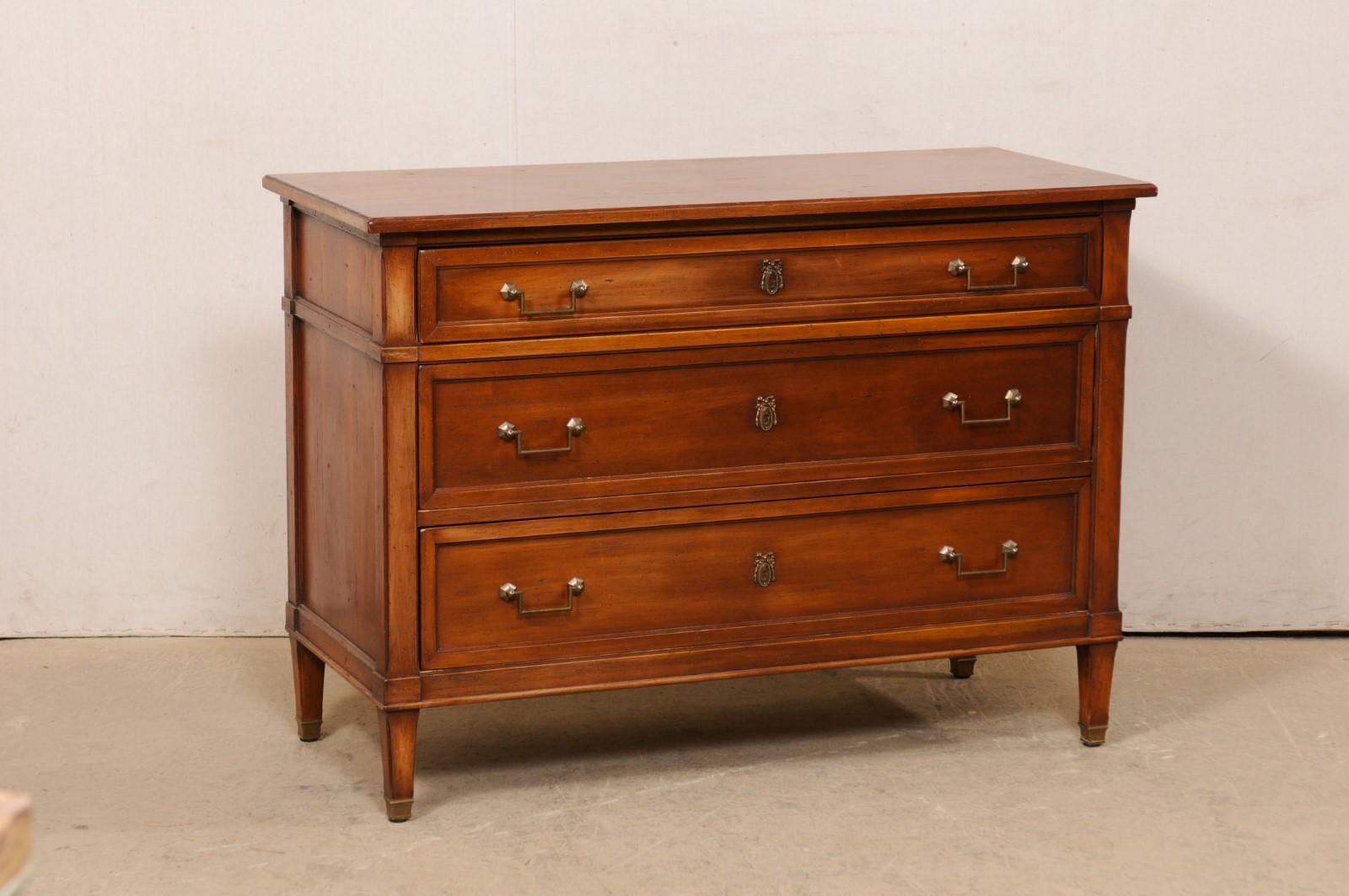 A French chest of drawers, designed in clean linear lines, circa 1940's. This wooden commode from France has three dovetailed and graduated drawers, fitted with Neoclassic style rectangular pulls flanking a wreathed escutcheon at center. The chest