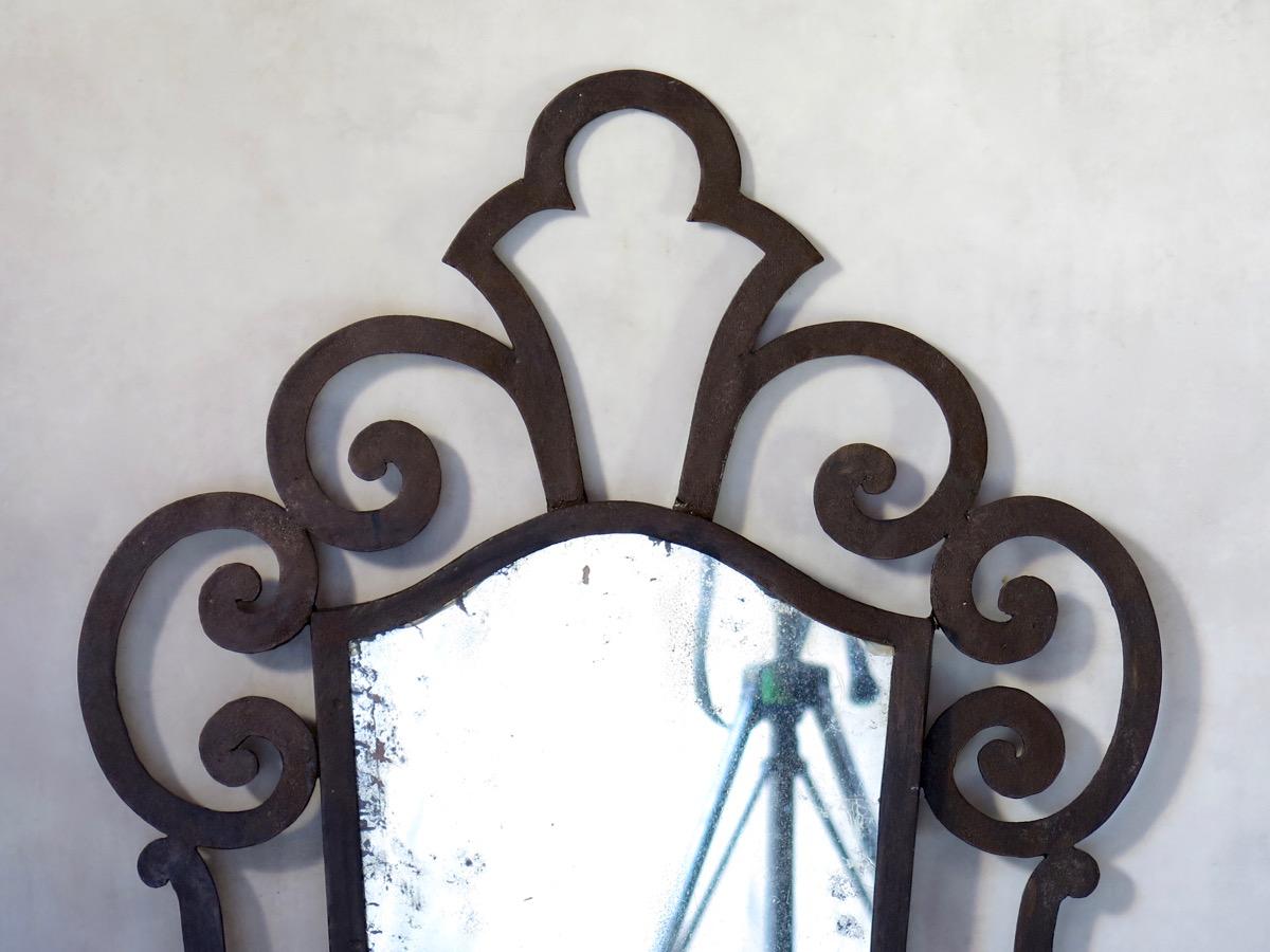 Baroque 1940s style wrought iron mirror. The looking glass has a peeling back. Wooden back.