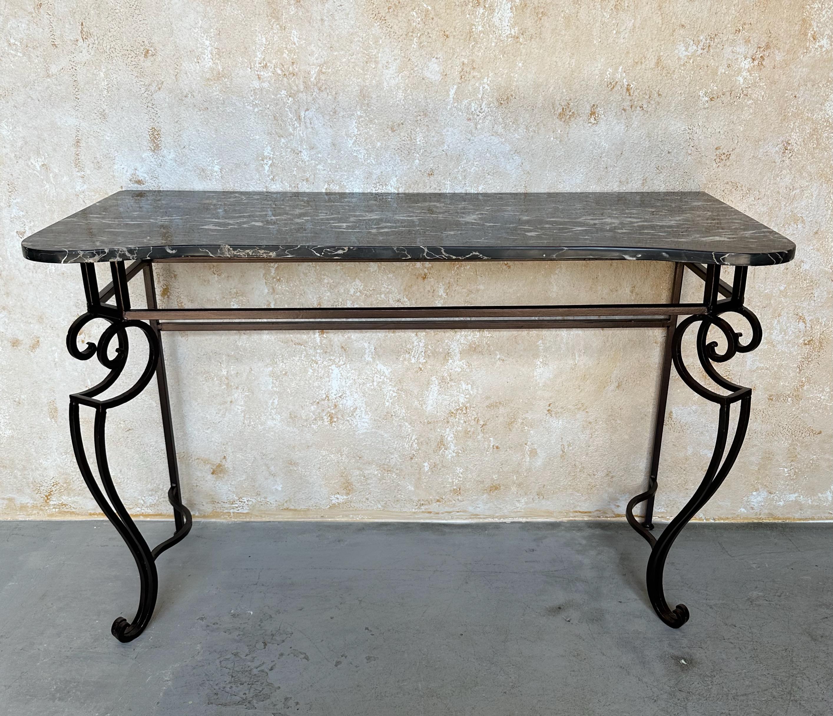 An elegant French iron console with marble  from the 1940s. The  wrought iron base features intricate scrollwork, recently finished in a deep bronze or black hue, creating a dramatic foundation. The beautiful marble top, with its prominent veining
