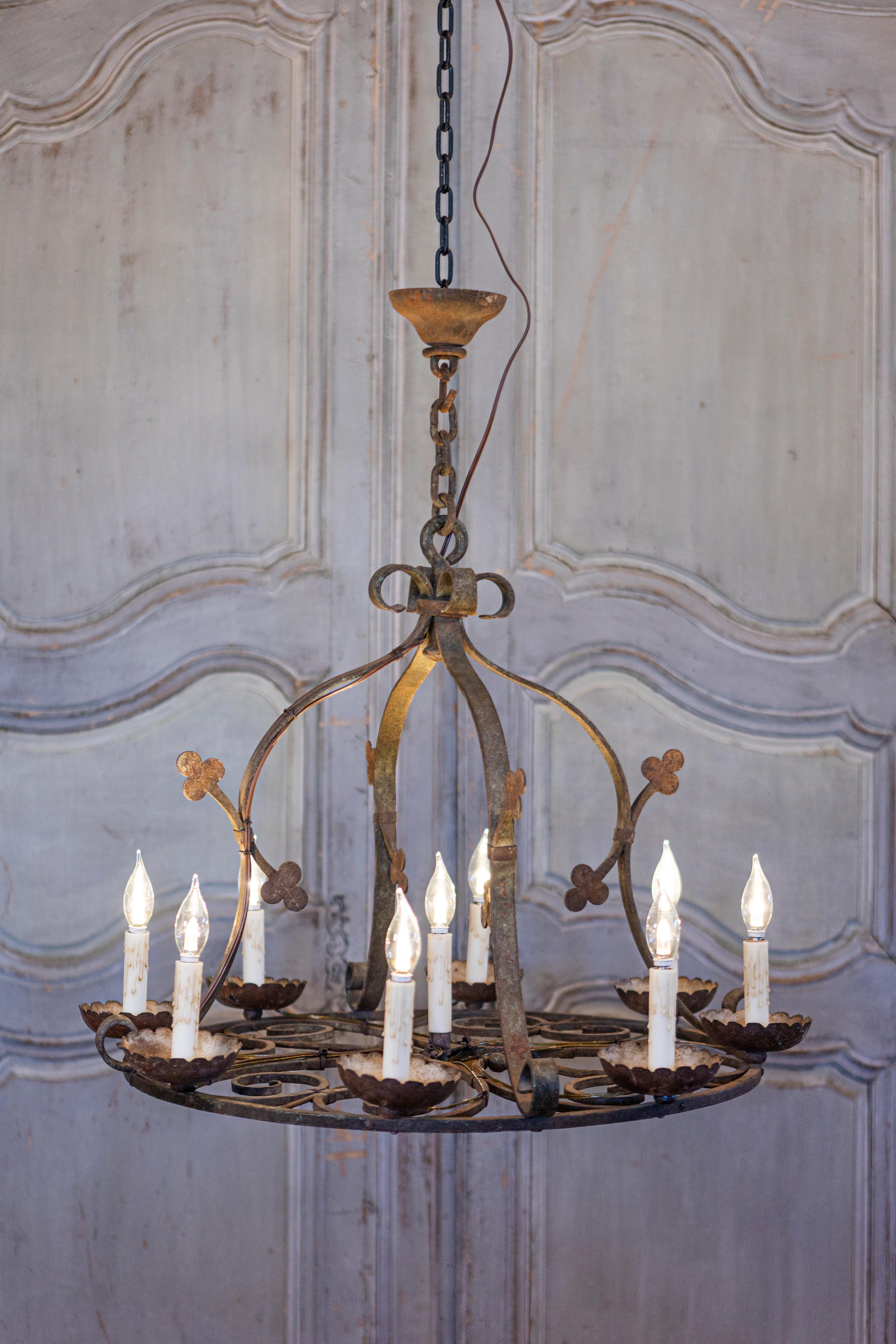 A French wrought iron chandelier from circa 1940 with nine lights and clover leaf motifs, professionally rewired for the USA. This French wrought iron chandelier from circa 1940 captures the essence of rustic elegance, characterized by its