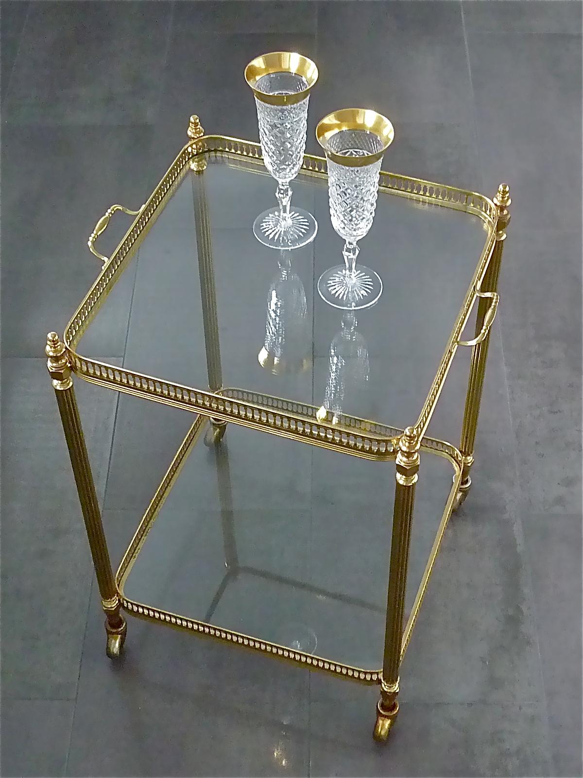 Amazing vintage bar cart, drinks serving trolley or side table on four small wheels made by Maison Baguès Paris, France, circa 1950. It is made of patinated brass with overall nice details, brass metal and clear slightly green tinted glass. It has