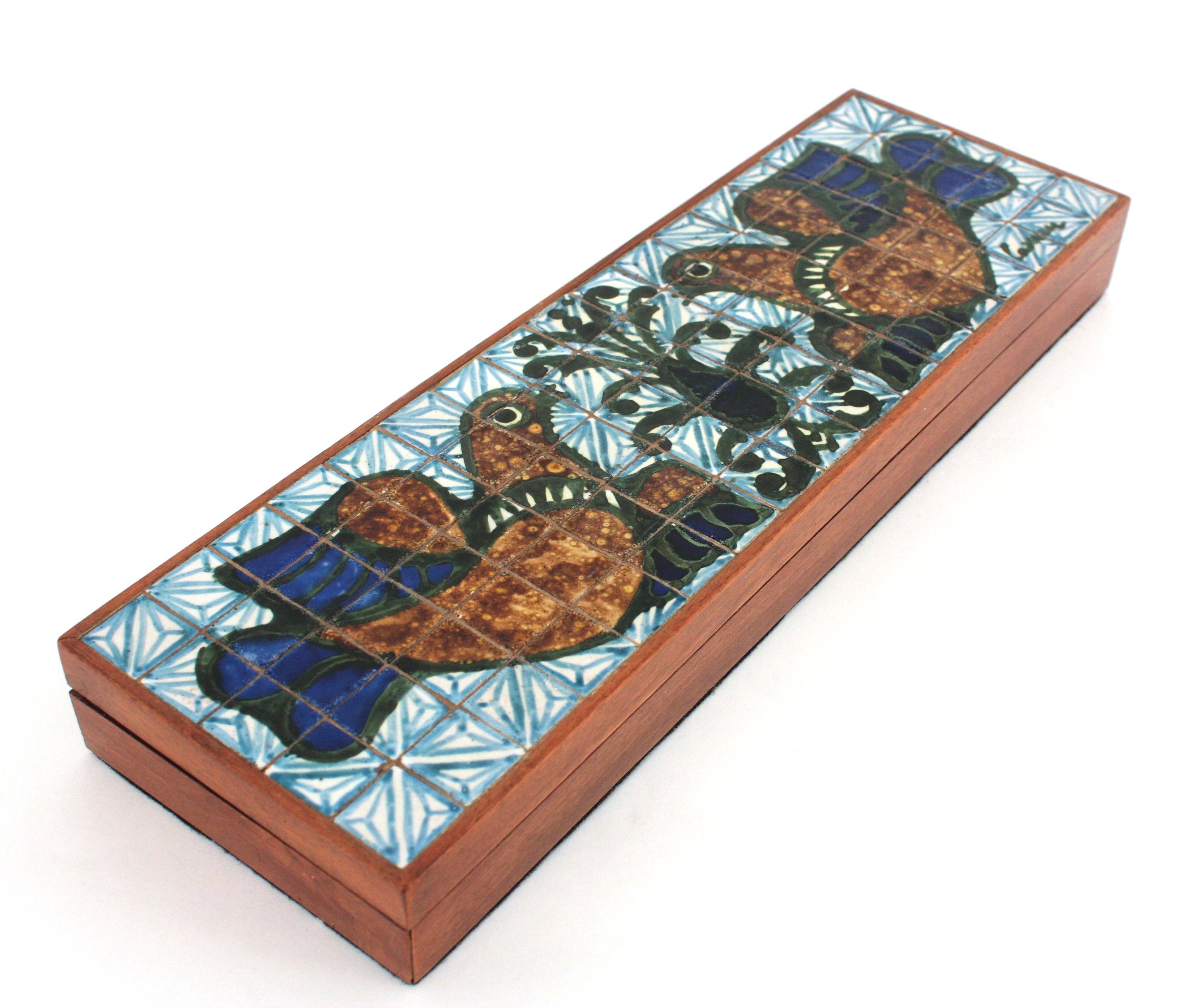 Mid-Century Modern hinged wooden box with colorful birds ceramic tiles top, France 1950s.
This exquisite vintage rectangular box is all constructed in wood. Beautiful hand-painted tile top with birds motifs and brass hinges. 
This trinket box in in
