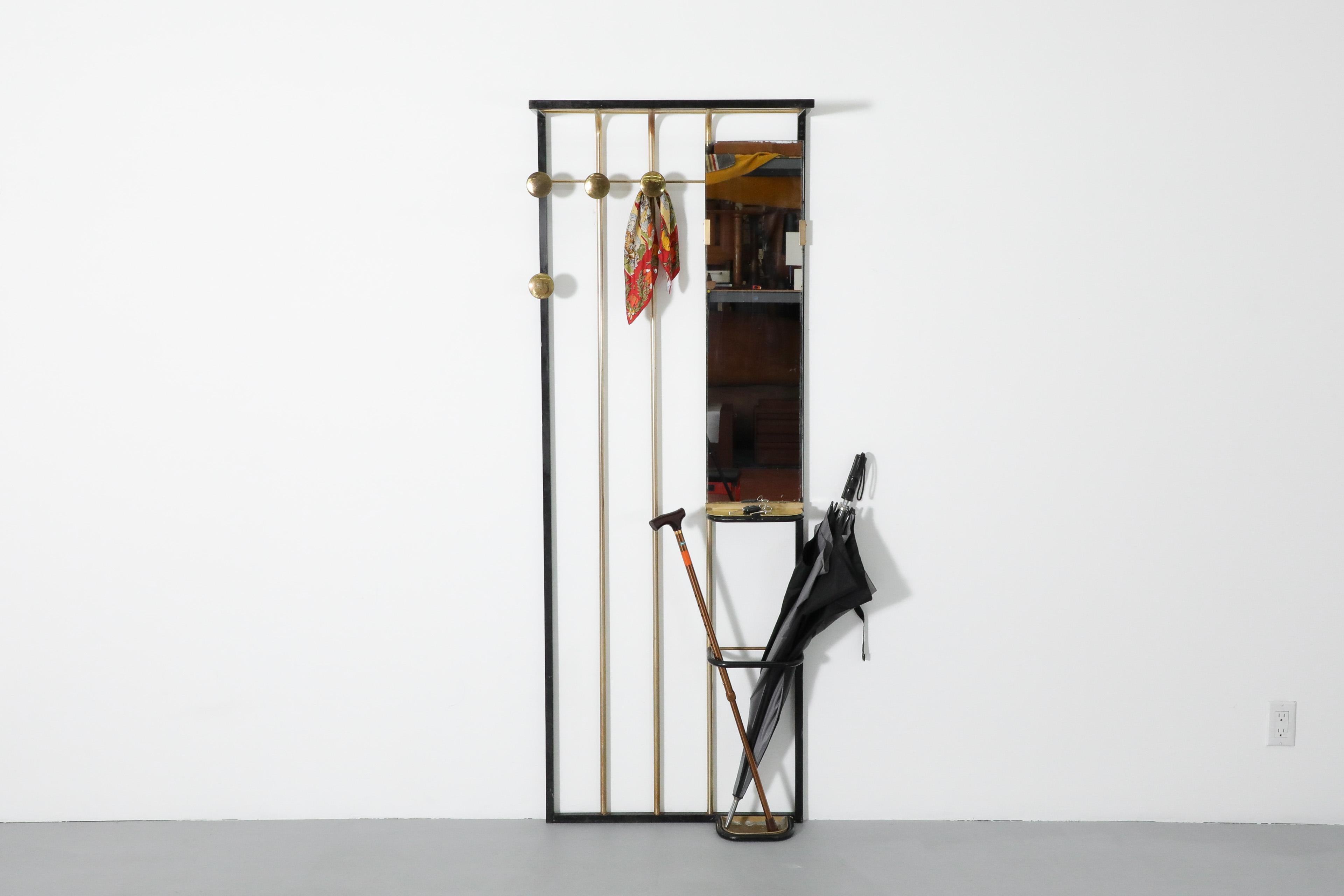 Elegantly designed, French Mid-Century, brass and black enameled metal, wall mounted coat rack. Outfitted with a mirror, brass coat hooks, an attached umbrella stand and a (newly made) custom brass key shelf this is not only a beautiful piece but a