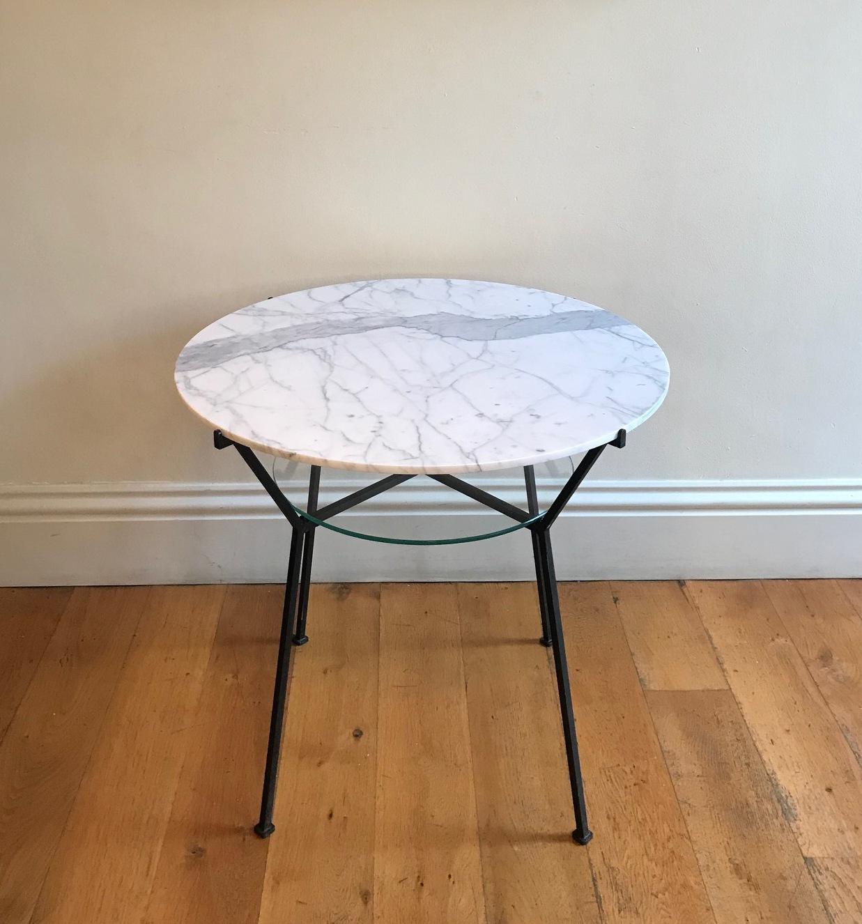 A painted black iron two-tier side table. With circular Carrara marble top (replaced) and clear glass shelf. Designed by the French, 20th century designer Charles Ramos.