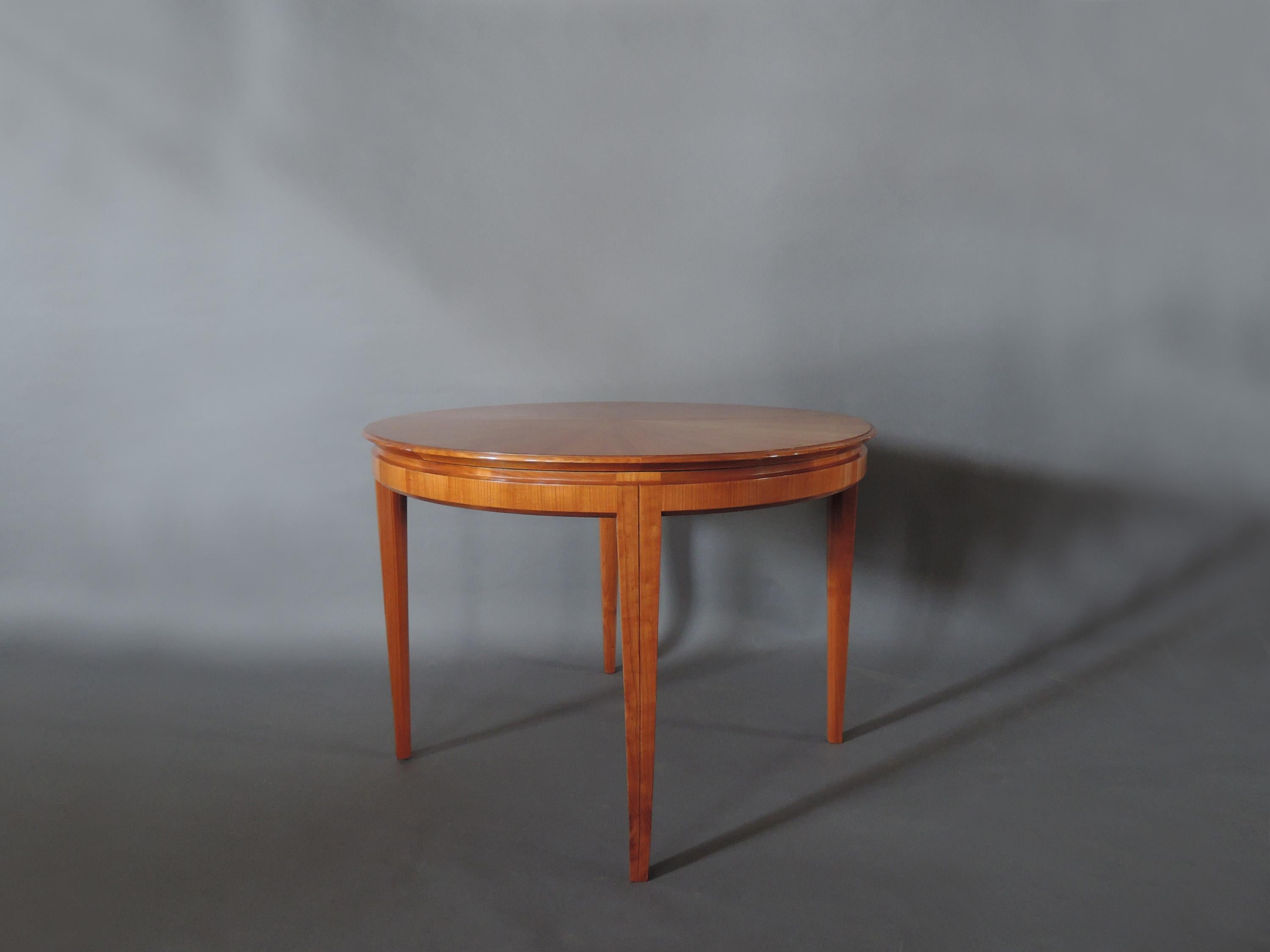 A fine French midcentury cherry round dining table divisible into two half moon consoles, with a very ingenious system that makes possible one or two center extension leaves (to be made, not included in price).