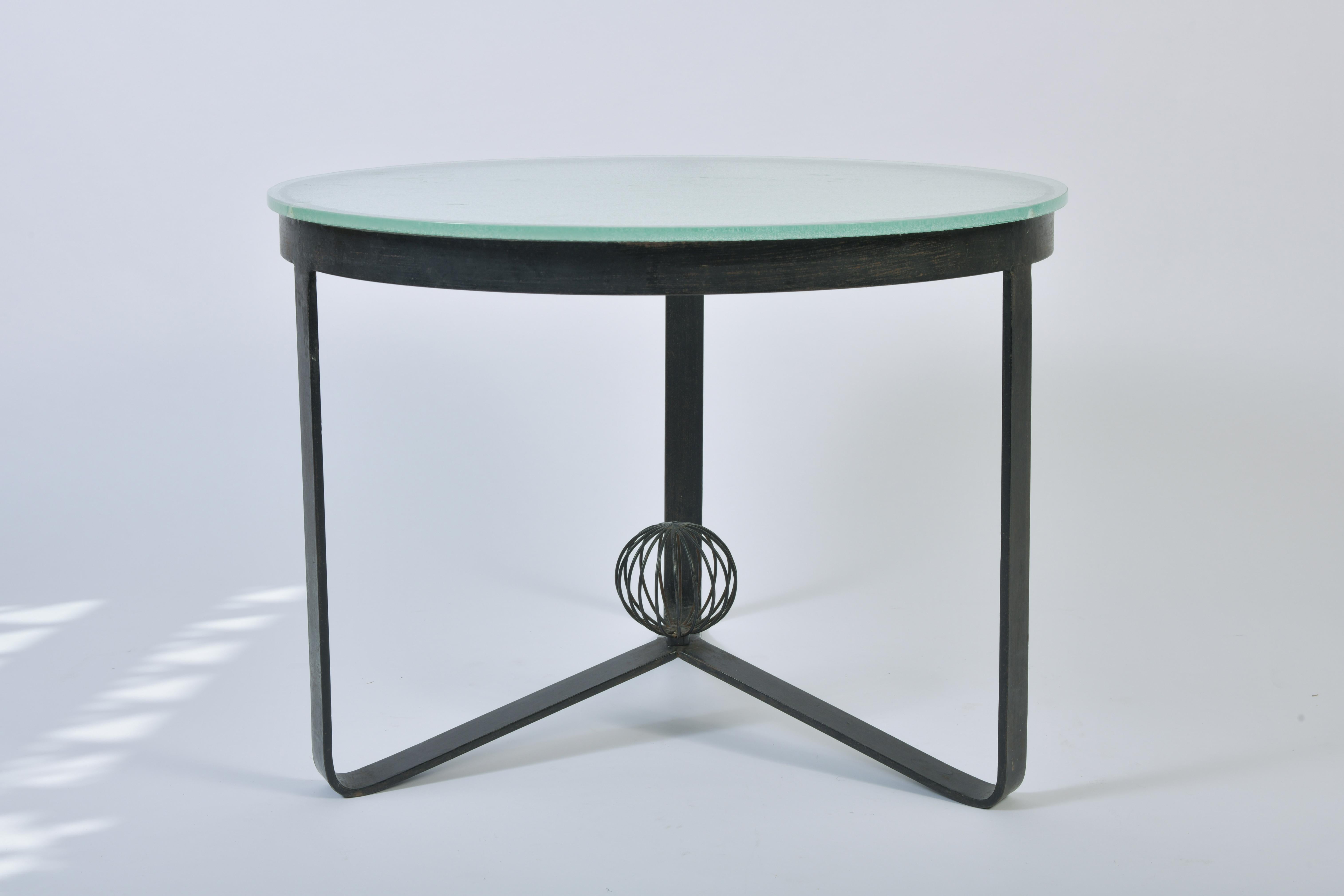 A glass top and iron circular coffee table, the tripod base joined together with an open spherical finial, France, circa 1950.
 