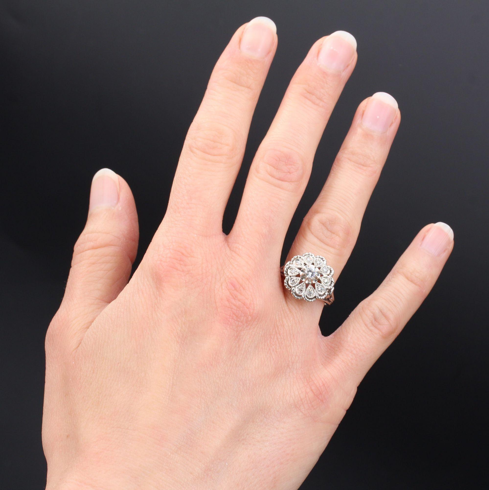 Anello in oro bianco 18 carati, marchio di fabbrica con testa d'aquila.
Rappresentando un anello a fiore, è decorato al centro da un moderno diamante taglio brillante, con petali incastonati da diamanti taglio 8/8, il tutto delimitato da un cordone