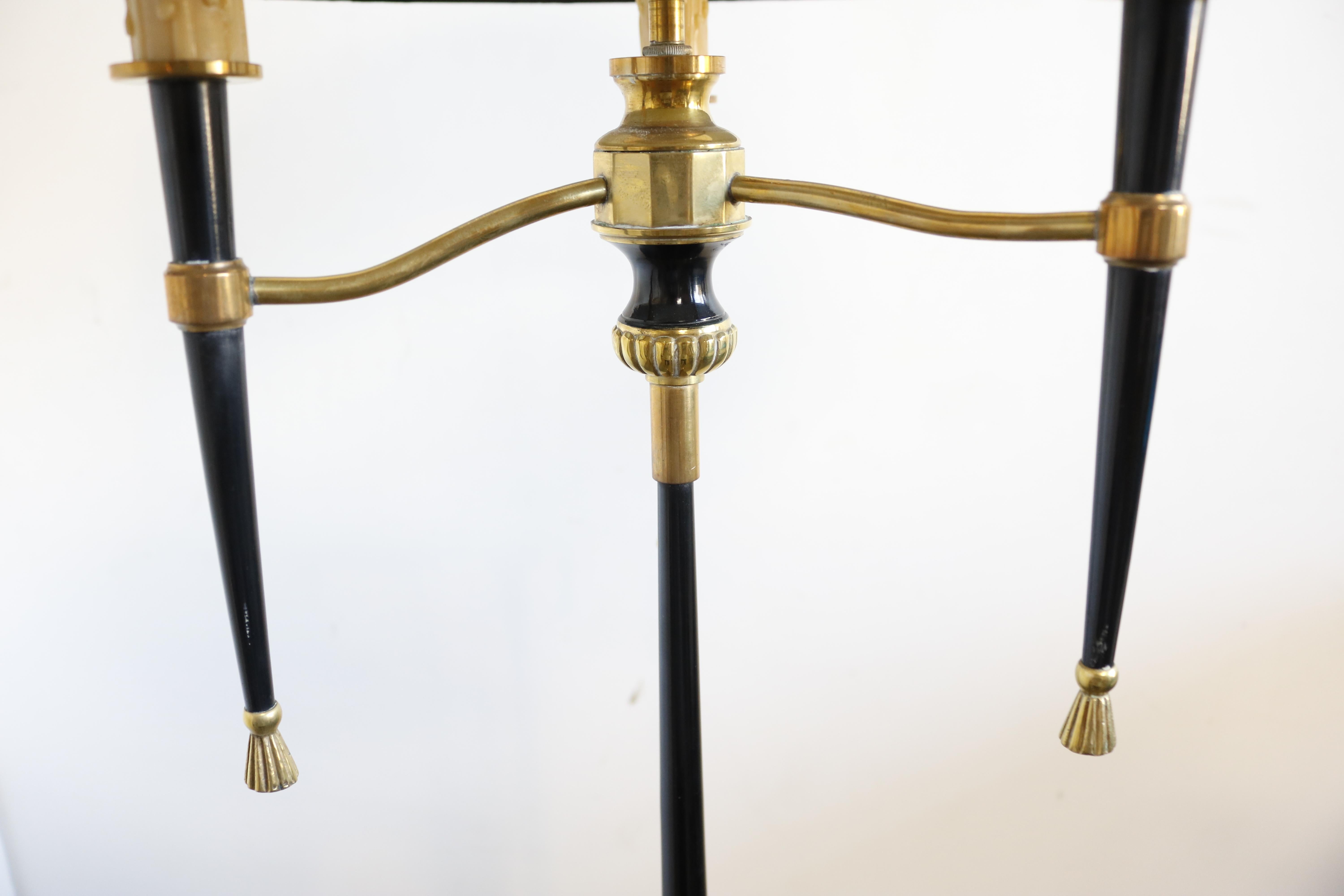 This 1950s floor lamp from France features a brass base, supporting a thin black column decorated at the middle with brass rosettes. At the top, a trio of faux candles on tapered holders provides space for three lightbulbs, encased by a custom-made