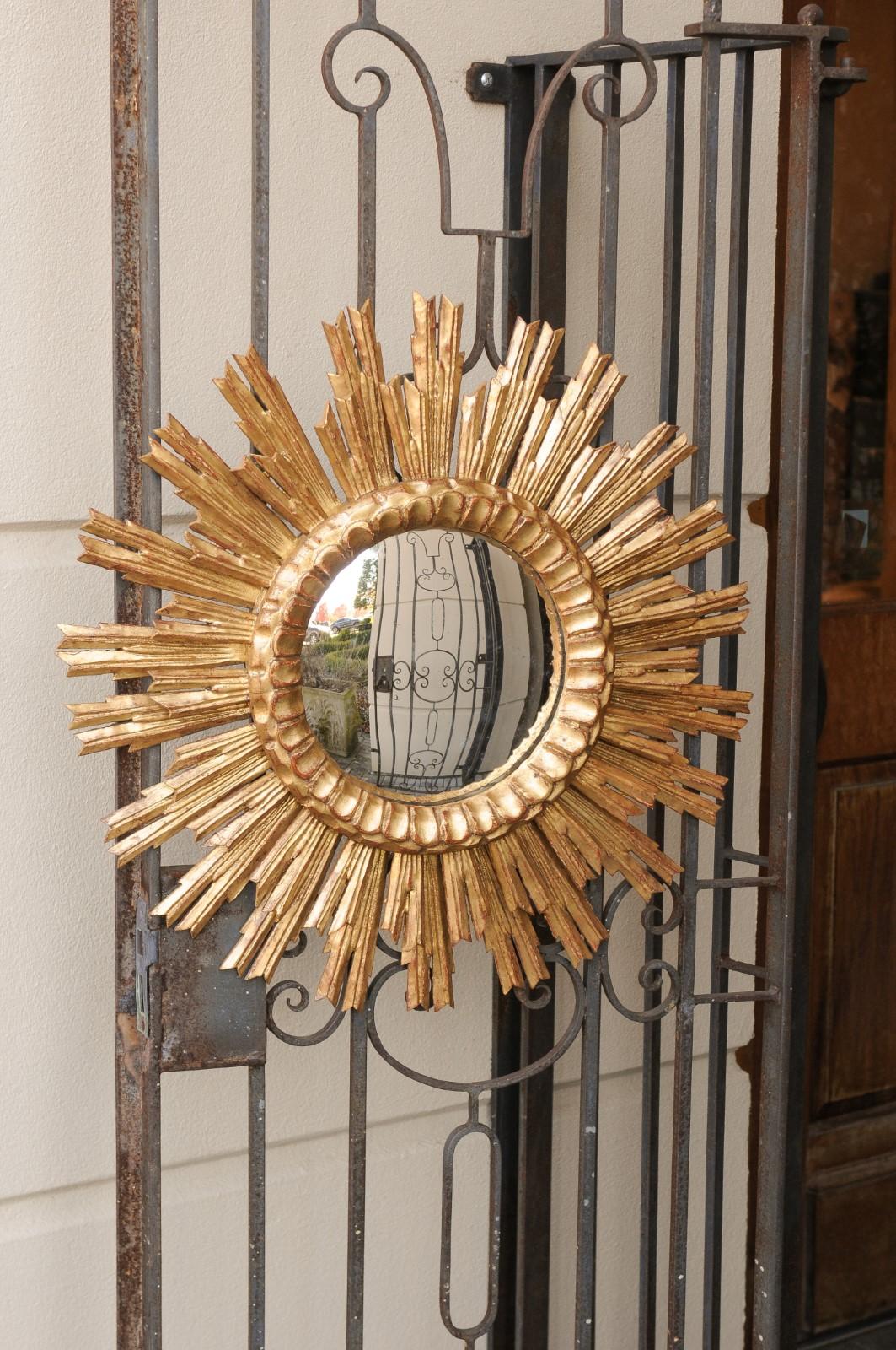 A vintage French giltwood sunburst mirror from the mid-20th century, with layered rays and convex mirror plate. Born in France during the midcentury period, this exquisite sunburst mirror features a convex central mirror plate providing a charming