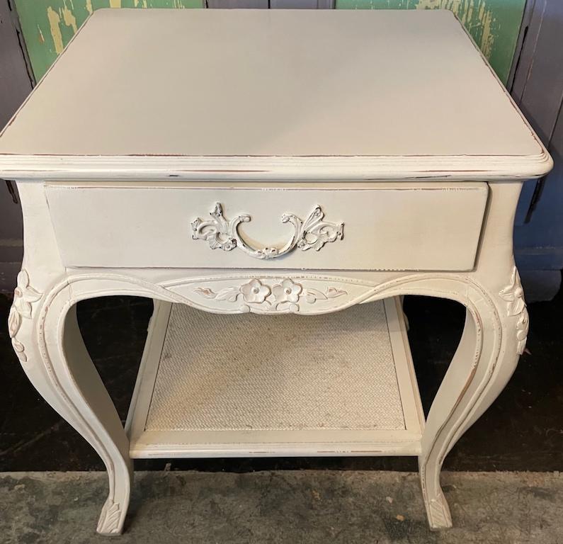 This is a small white hand-painted vintages nightstand. It has hand-carved cabroile legs. Also there is one upper drawer and a small lower wicker shelf.