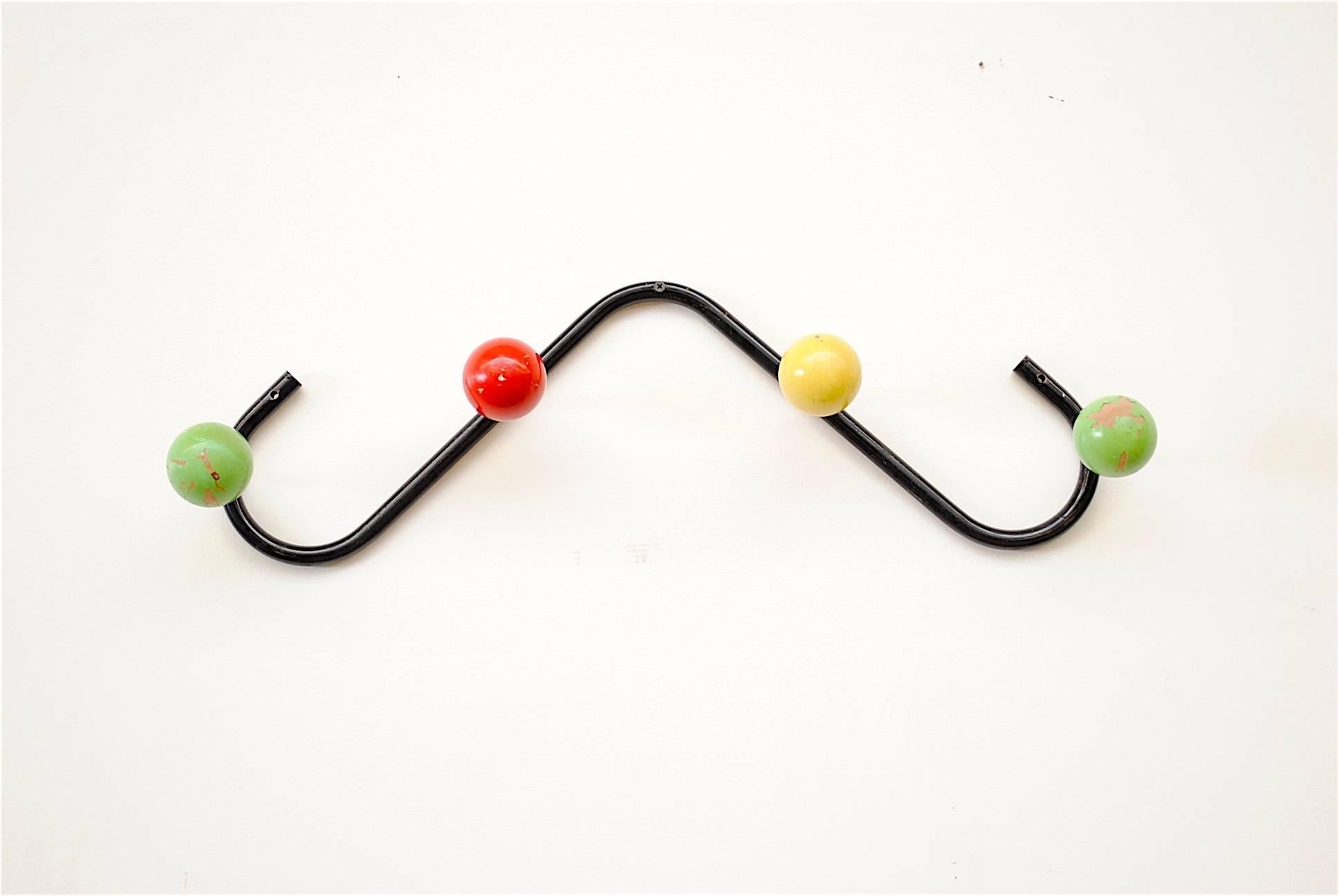 Black enameled metal wall-mounted coat rack with whimsical multicolored wood ball hooks in green red and yellow. Frame and wood have visible wear with clear paint loss.