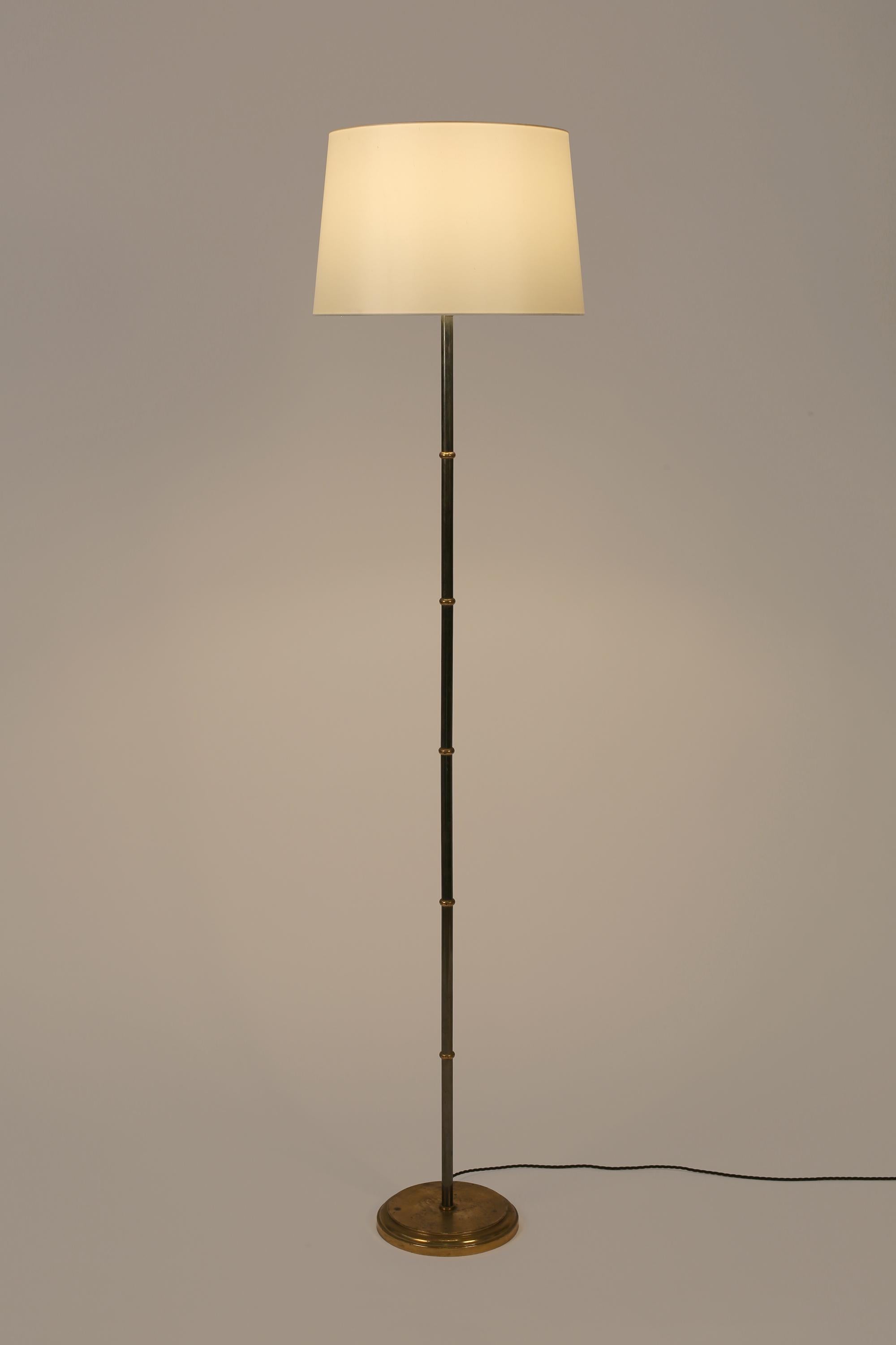 A gunmetal and patinated gilt-brass floor lamp with stylised ‘faux bamboo’ stem and circular, spun base. French, c. 1950s. Supplied with an off-white dupion silk shade.