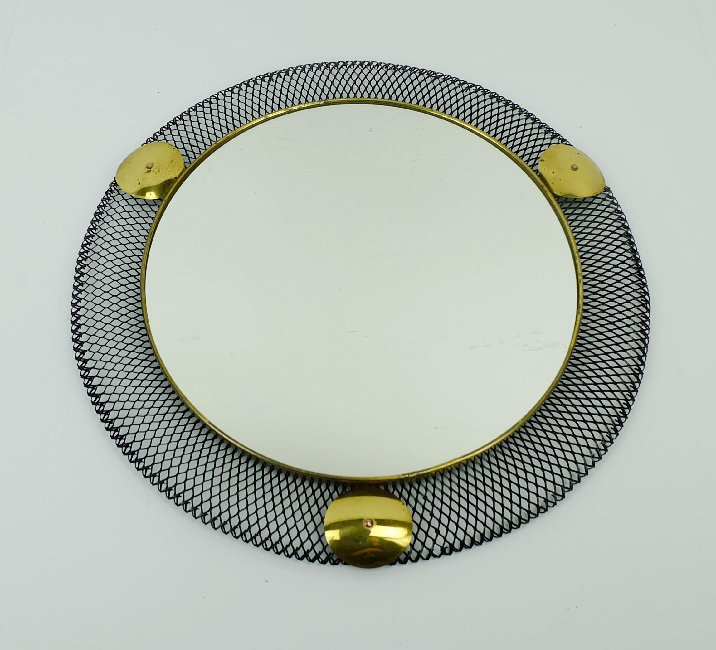Miroir mural très décoratif du milieu du siècle dernier. Le cadre est en treillis métallique noir et en laiton. Le miroir lui-même est également encadré de laiton. 

Dimensions : diamètre 13 3/4