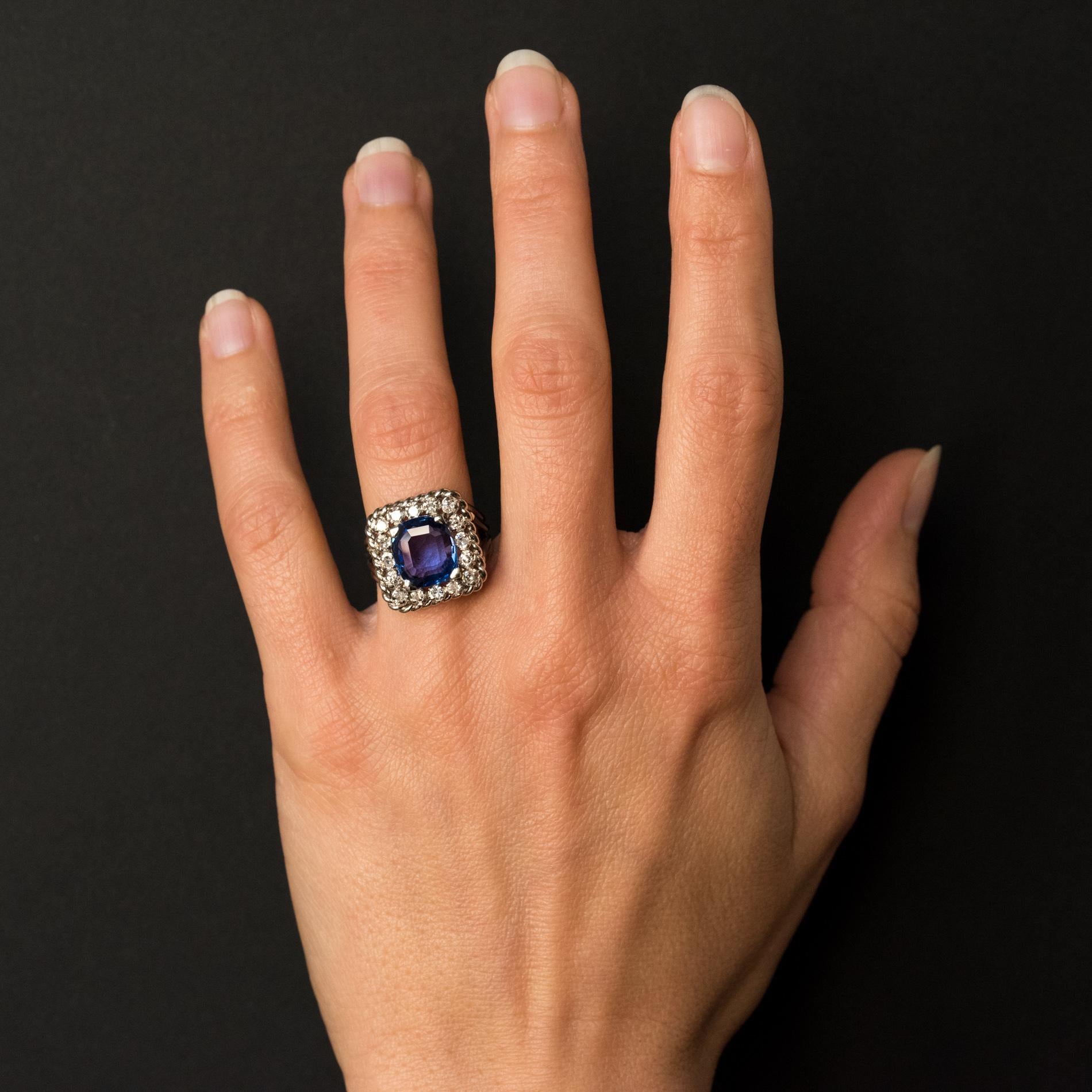 Ring aus Platin, Hundekopfpunze.
Dieser rechteckige, erhabene Retro-Ring ist mit 4 Klauen eines blauen Saphirs im Kissenschliff besetzt, der von 16 Diamanten umgeben ist, die alle mit einer Drehung eingefasst sind. Der Ring besteht aus 4 Fäden, die