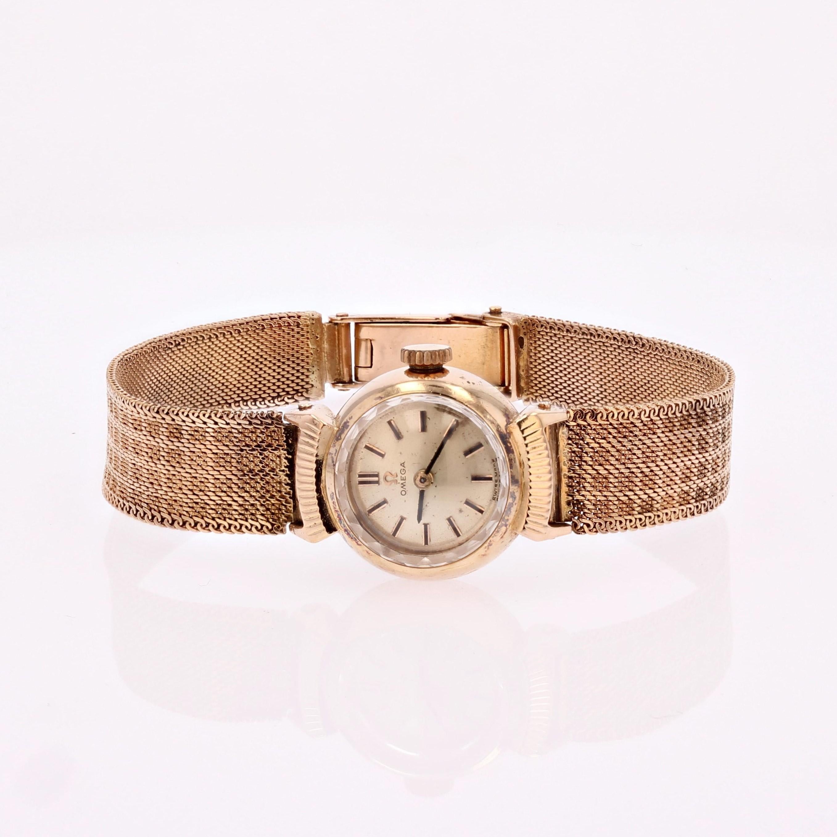 Watch in 18 karat yellow gold, eagle head hallmark.
The case is round in smooth gold, with “Omega Swiss Made” in the center on a brushed-finish gold background. The bracelet, also in yellow gold, falls to the clasp and is made of woven mesh. The