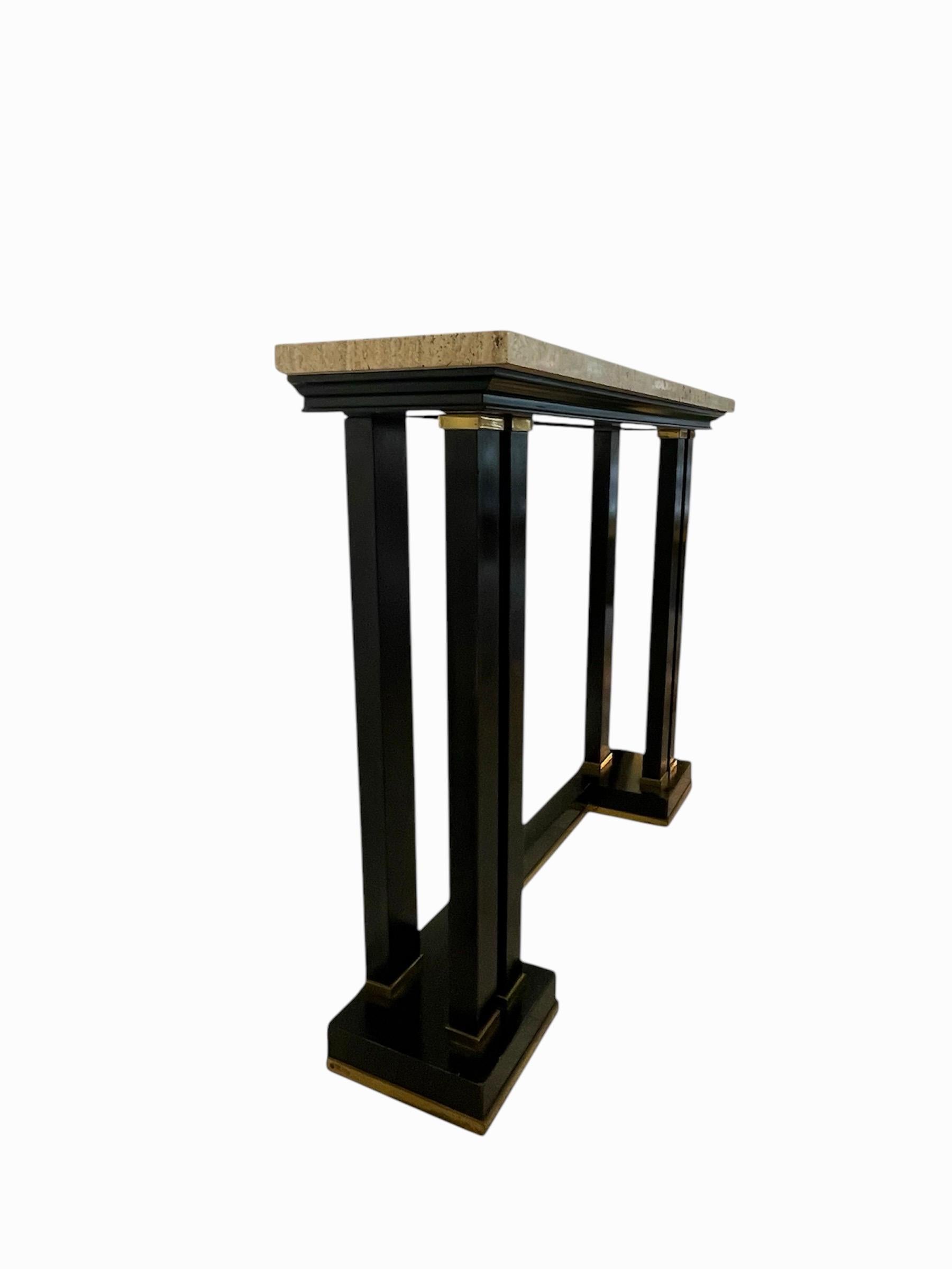 Elegant and sleek console table designed by Maison Jansen, Paris C 1960. 
In the Neo Classical style with black lacquered pillars with beautifully conceived brass collars and a plinth supporting an original travertine top. 
The console is classical