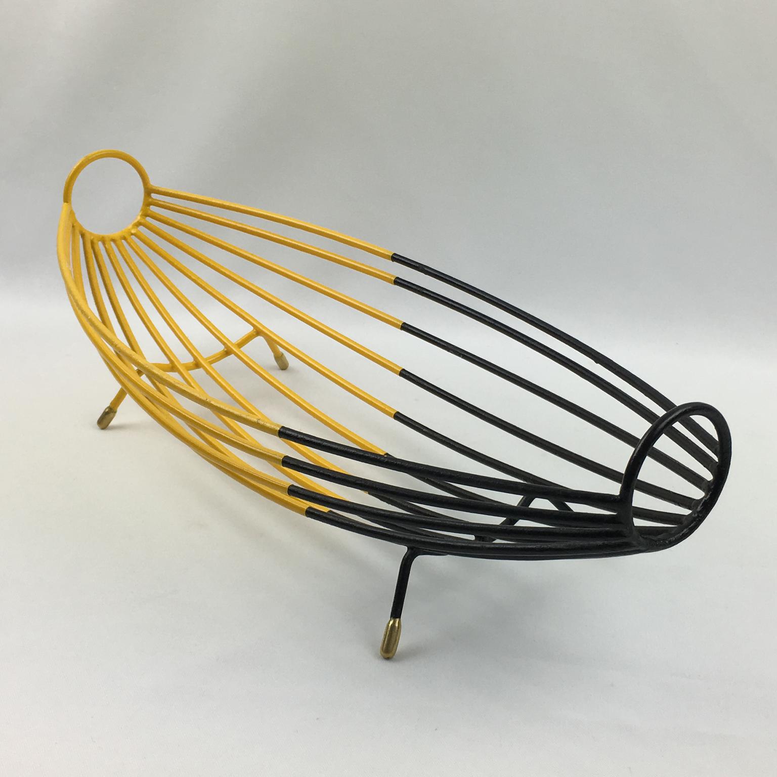Handsome 1960s modernist metal fruit bowl or basket or centerpiece. Black and yellow lacquered paint patina with polished brass feet. Elongated hammock shape with thin metal rods. Bi-color geometric design. No visible maker's mark.
Measurements: 15
