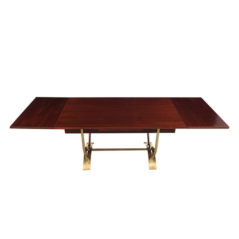 This sleek 1960's Modern Dining Table has been newly restored, made out of mahogany wood, and has been newly stained a rich mahogany color with a lacquered finish. The writing table has a 20-inch wide pullout leaf on each side, and rests on a solid