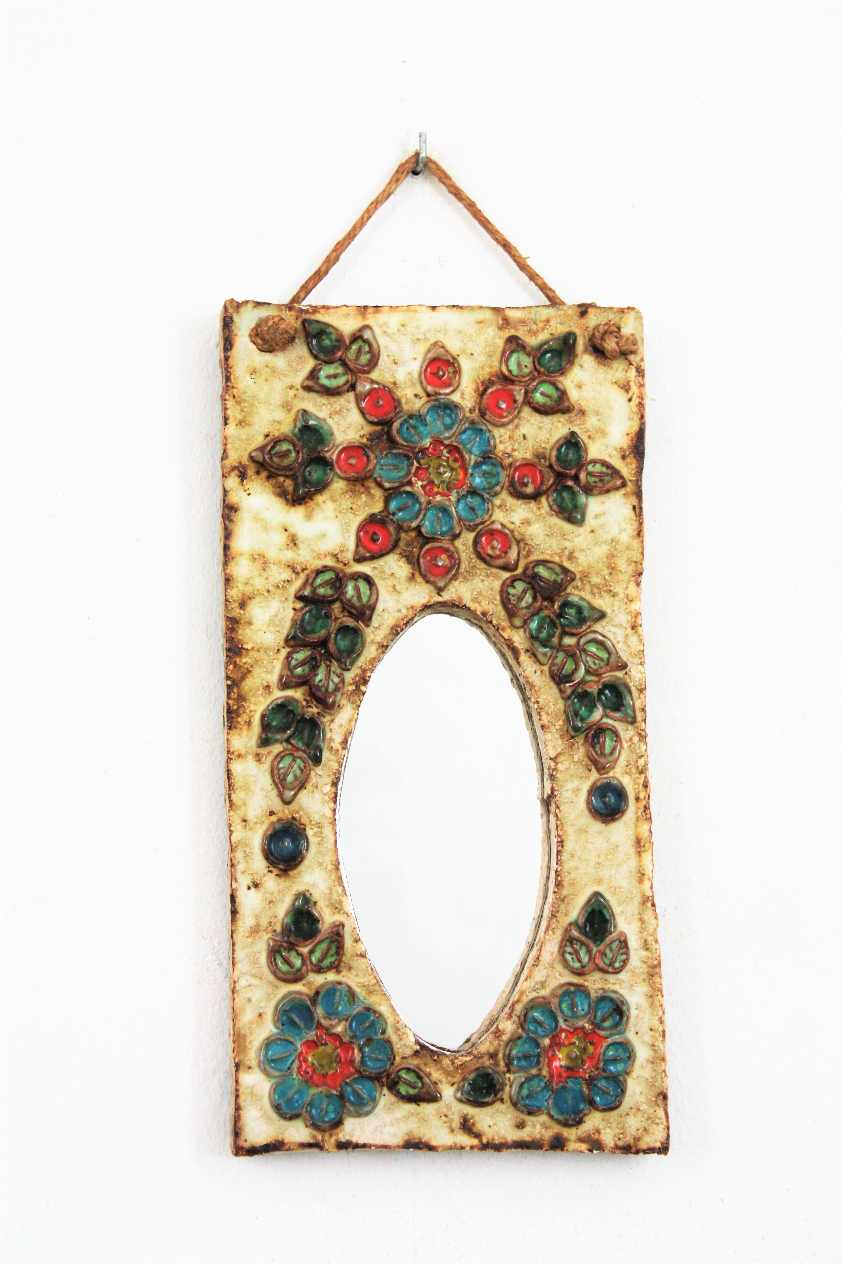 A glazed ivory color ceramic mirror with colorful flowers decorating the frame. Attributed to La Roue-Vallauris. France, 1950-1960.
This pretty beautiful mirror has midcentury and rustic accents. Small flowers in orange and blue colors and a