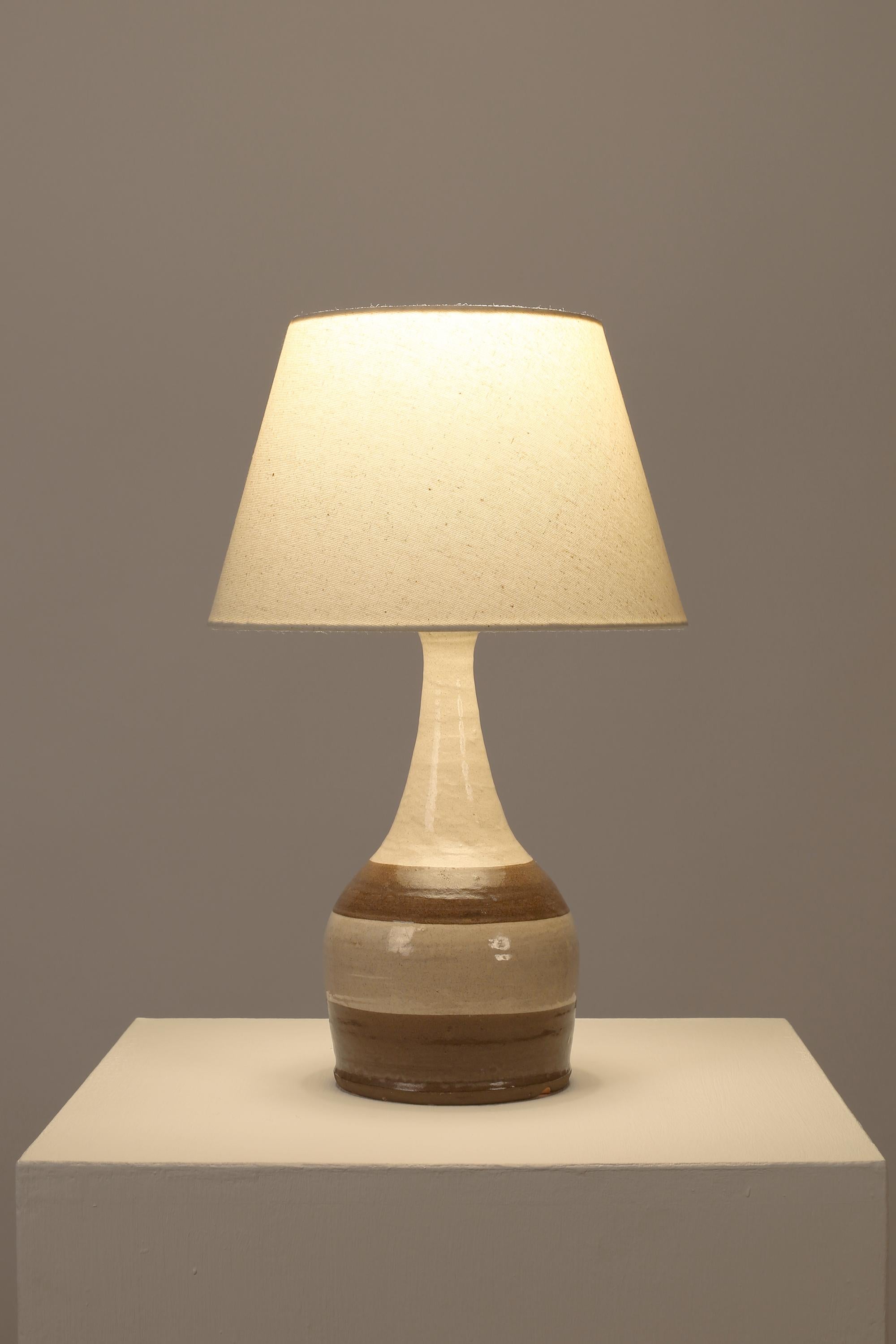 A terracotta table lamp of bottle-like form with speckled off-white and brown banded glaze, from the Poteries Du Marais - stamped. French, c. 1960s. Supplied with a tapered oatmeal fabric shade.