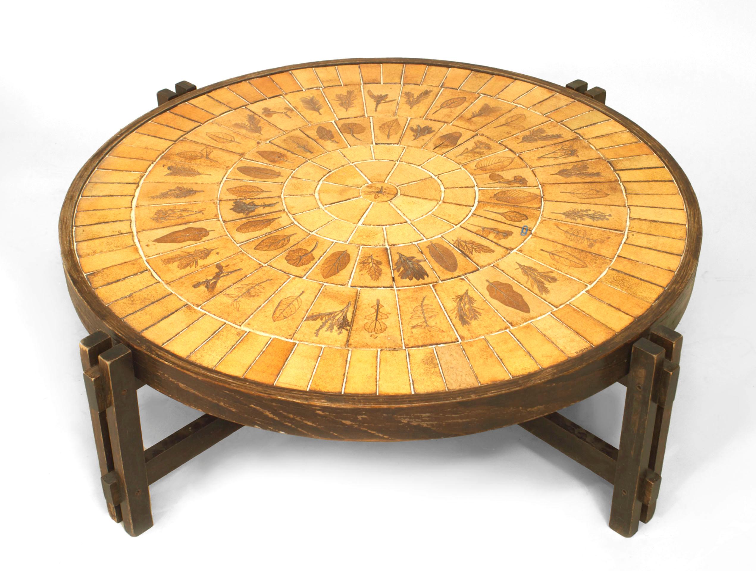 French Mid-Century (1960s) round coffee table with a stained four leg oak frame and stretcher supporting a beige ceramic sunburst design tile top with leaf decoration. (signed: ROGER CAPRON)
