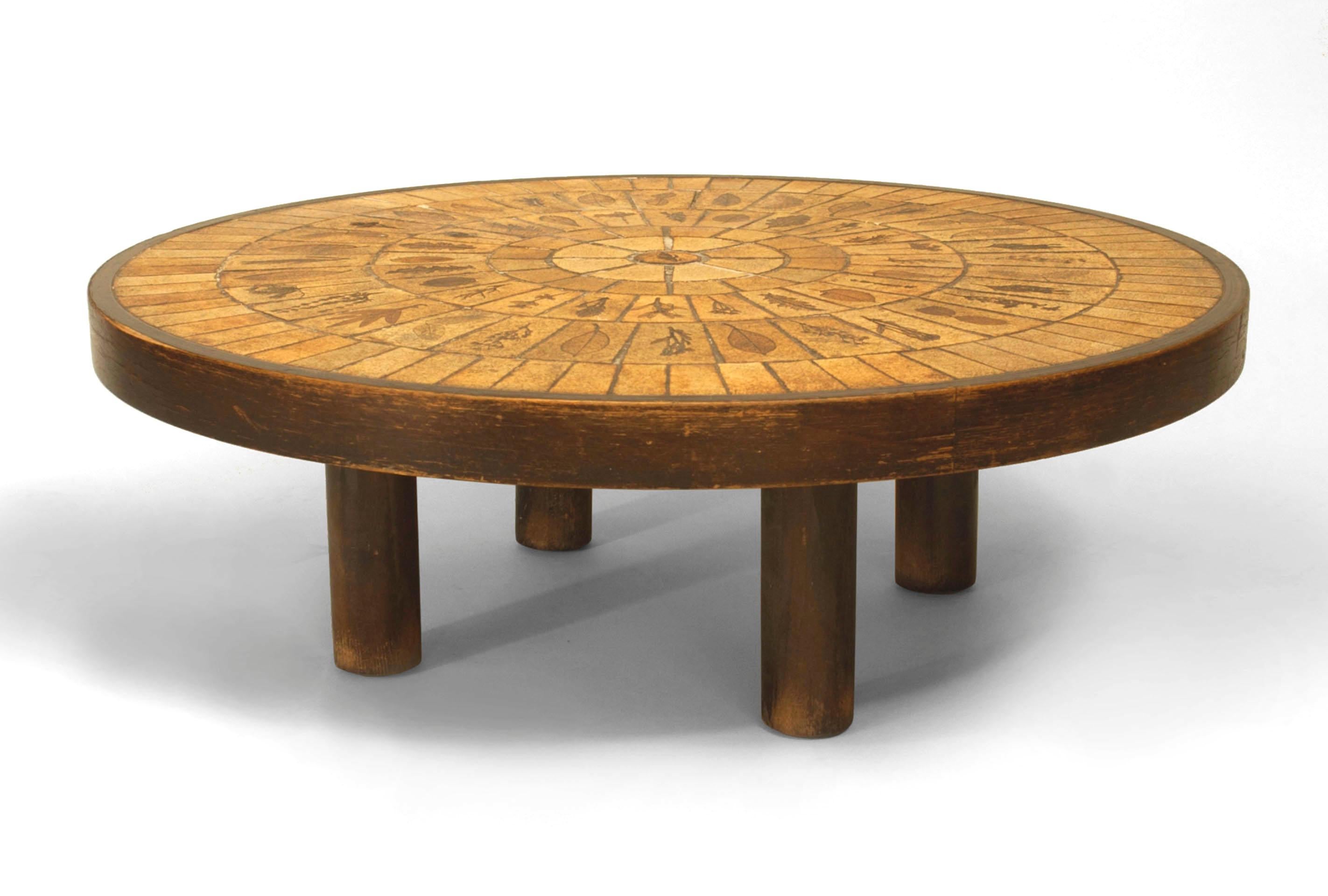 French Mid-Century (1960s) round coffee table with a round inset beige ceramic tile top with a sunburst design decorated with various leaves on a stained oak base. (signed: ROGER CAPRON)

