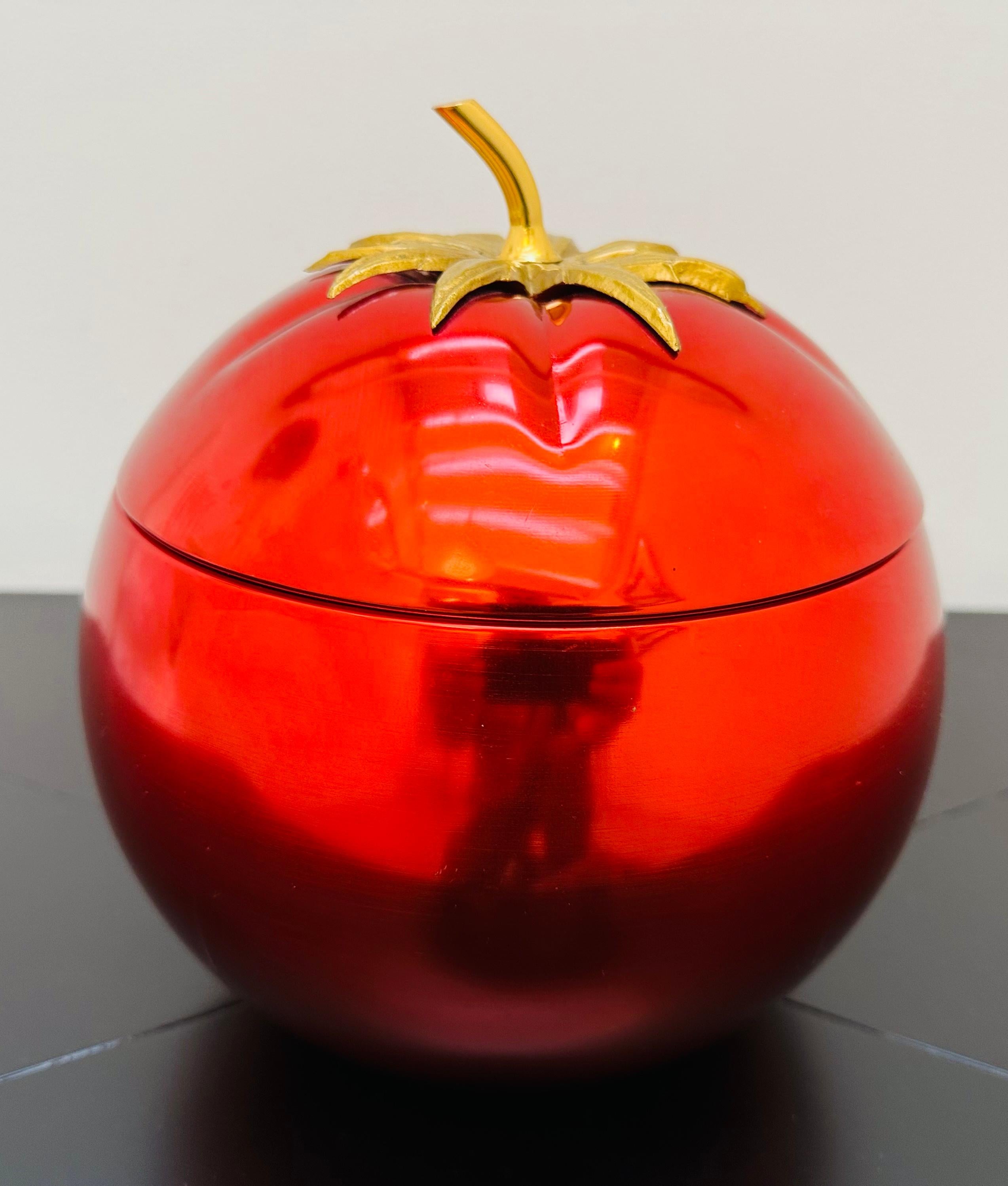 A fun and vibrant red anodised aluminium ice bucket in the shape of a tomato with a brass stalk and gold metal leaves.  Manufactured in the 1970s.  Marked: Modele Depose on the underside.  The interior which holds the ice inside is made from