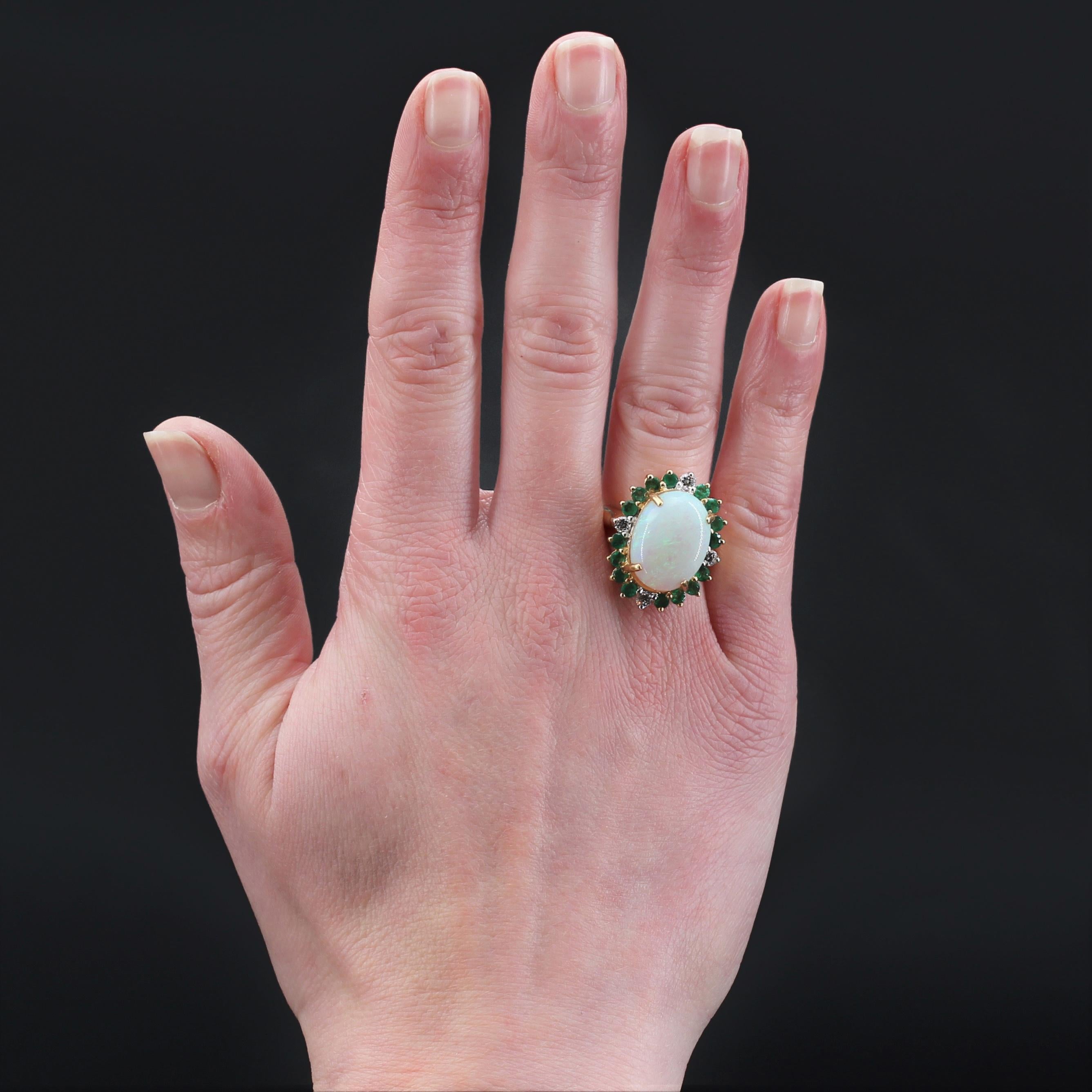Ring in 18 karat yellow gold, eagle head hallmark.
Important retro ring, it is set with 4 claws on its top of a cabochon opal with green-blue color games, surrounded by round emeralds and at the 4 cardinal points of a modern brilliant- cut