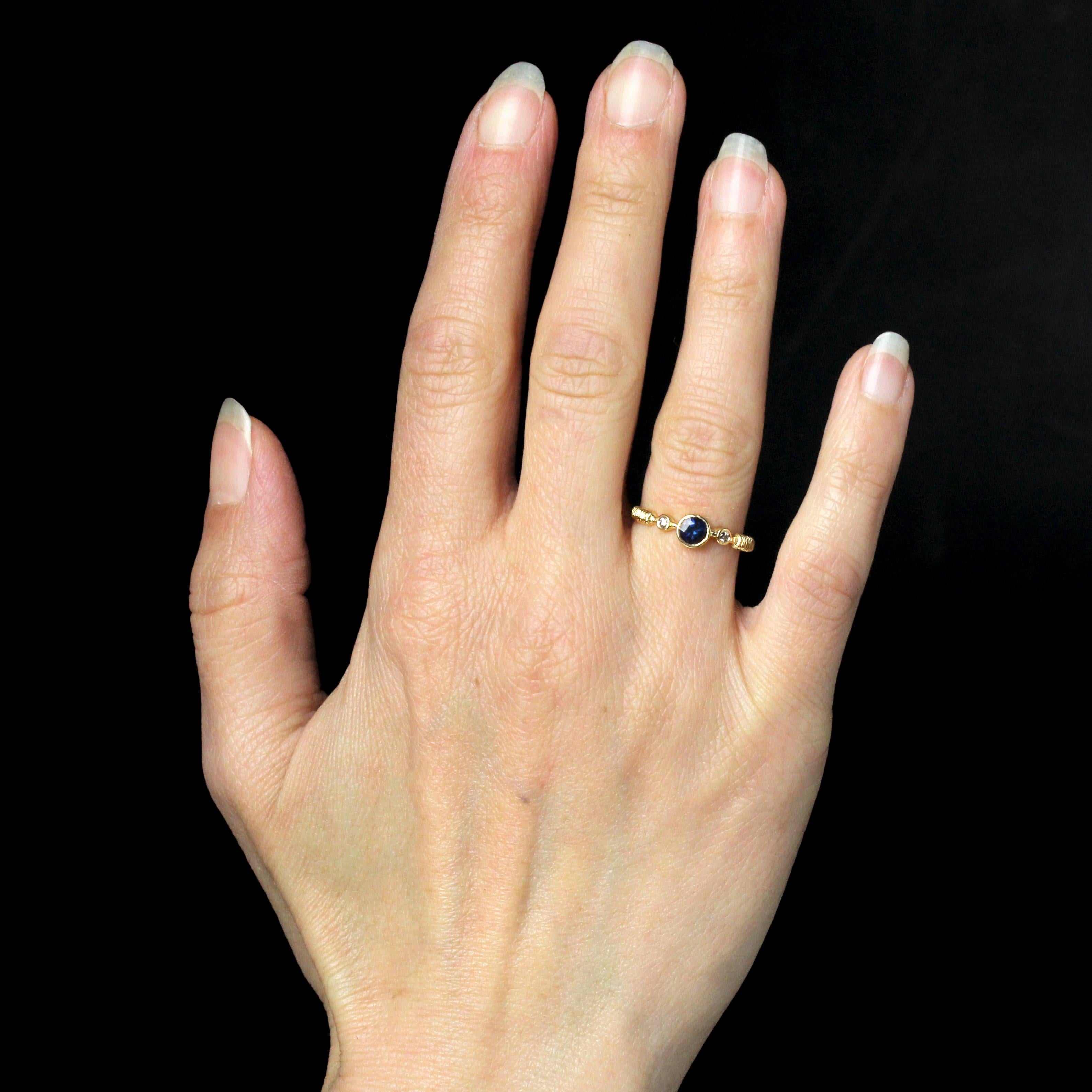 Bague en or jaune 18 carats, poinçon tête d'aigle.
Cette bague en or jaune fin présente un saphir rond en serti clos sur le dessus, flanqué de part et d'autre d'un diamant moderne de taille brillant également en serti clos. Le début de l'anneau est