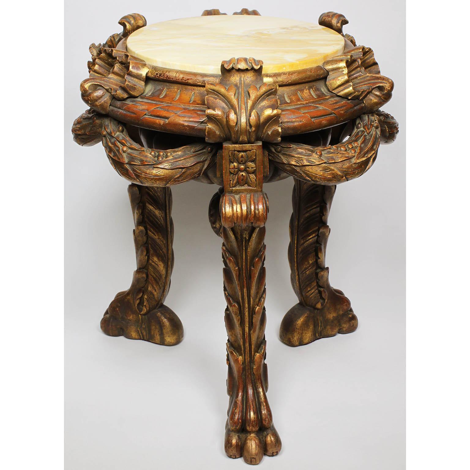 A French 19th-20th century Baroque Revival style giltwood carved three-legged pedestal stand with marble top. The circular gilt wood carved top with ribbons and wreaths with a circular veined yellow marble top, all raised on three acanthus cabriolet