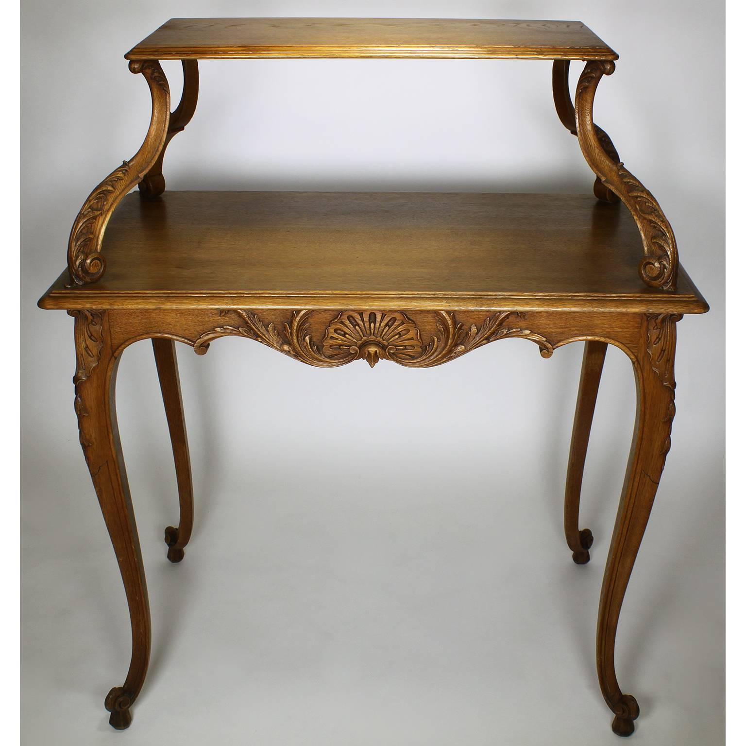 A French 19th-20th century Louis XV Style carved oak two-tier tea or dessert table. The tall and slender body with carved seashells on the apron, an upper shelf raised on four scrolled supports, all raised on four cabriolet legs with scrolled