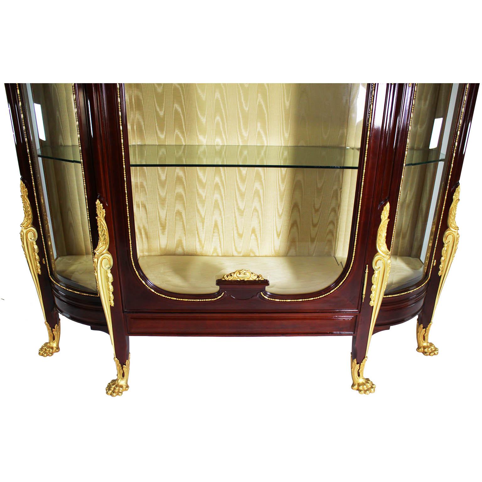 A Fine and Large French 19th/20th Century Louis XV Style Mahogany and Gilt-Bronze Mounted Three-Corps Vitrine Cabinet. The converted three door display case with twin bombé (rounded) side beveled glass doors and a central beveled glass door, all