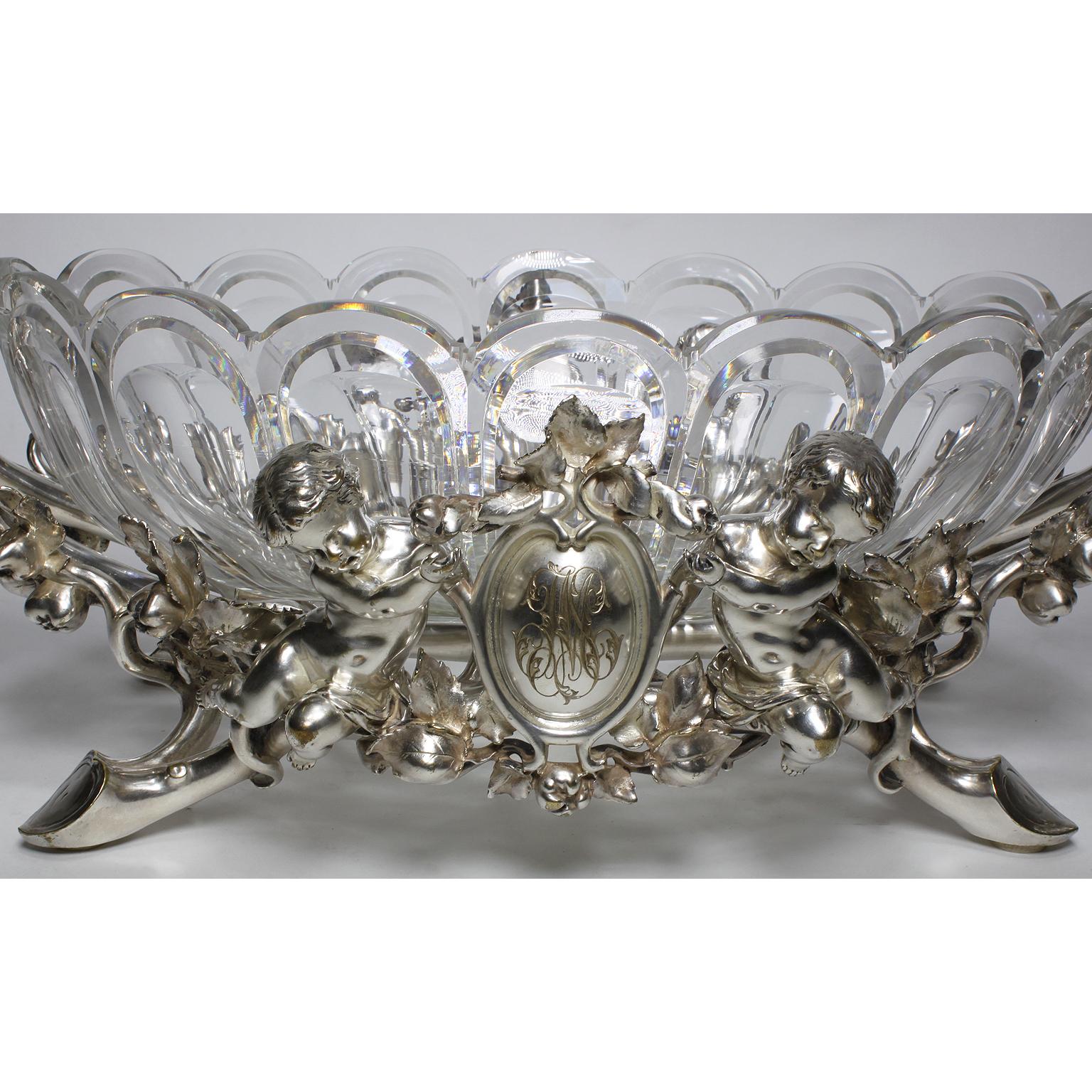 A very fine and palatial French 19th-20th century Christofle & Cie Louis XV style silvered figural centrepiece with a cut-glass scalloped centre-dish, attributed to Baccarat, and flanked by two Putti (Children), all on a pomegranate branch-form foot