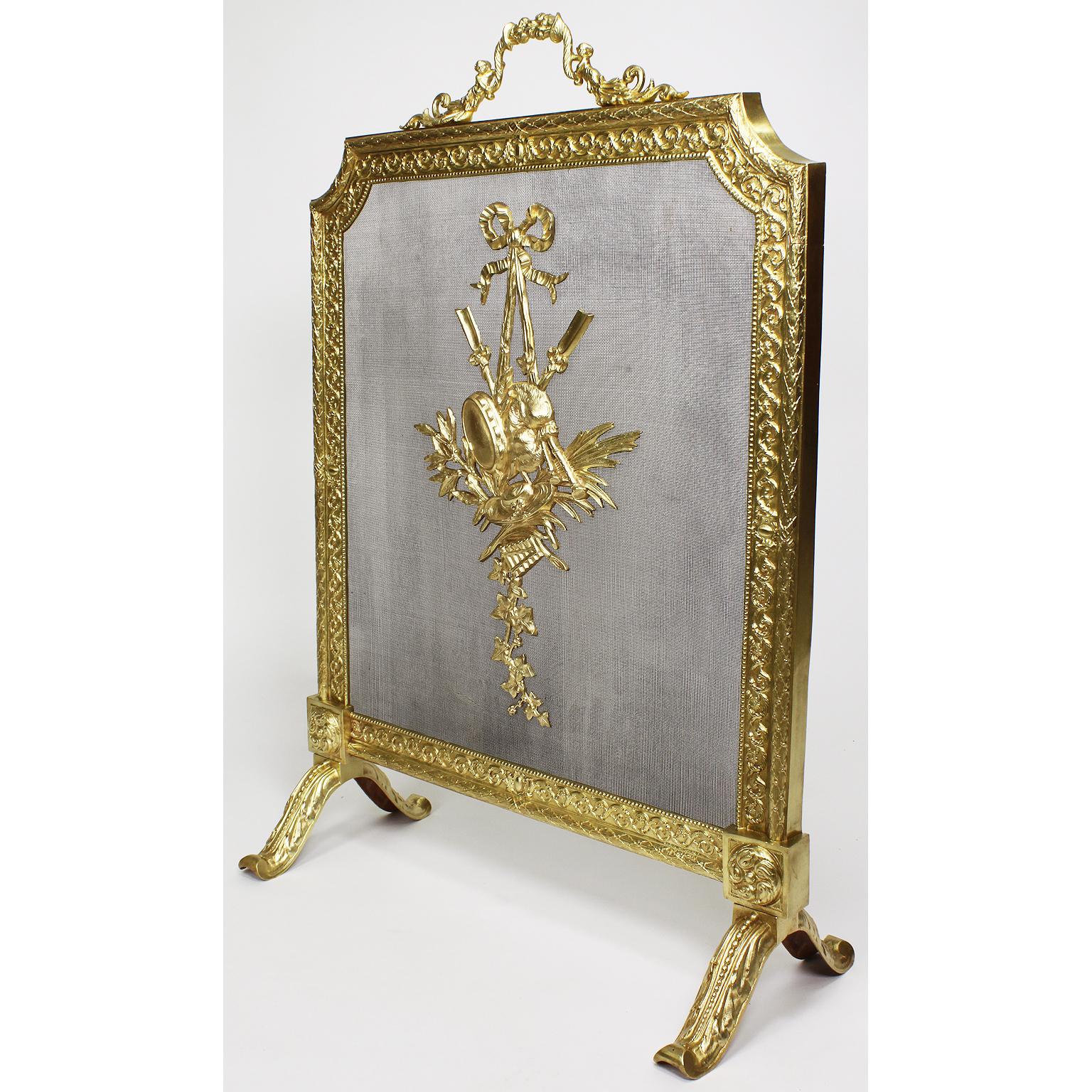 A French 19th-20th century Louis XVI style gilt metal fireplace screen. The ornately decorated screen topped with a twin-putti handle with a floral cornucopia, the floral border with a metal screen mesh centered with an allegorical shield