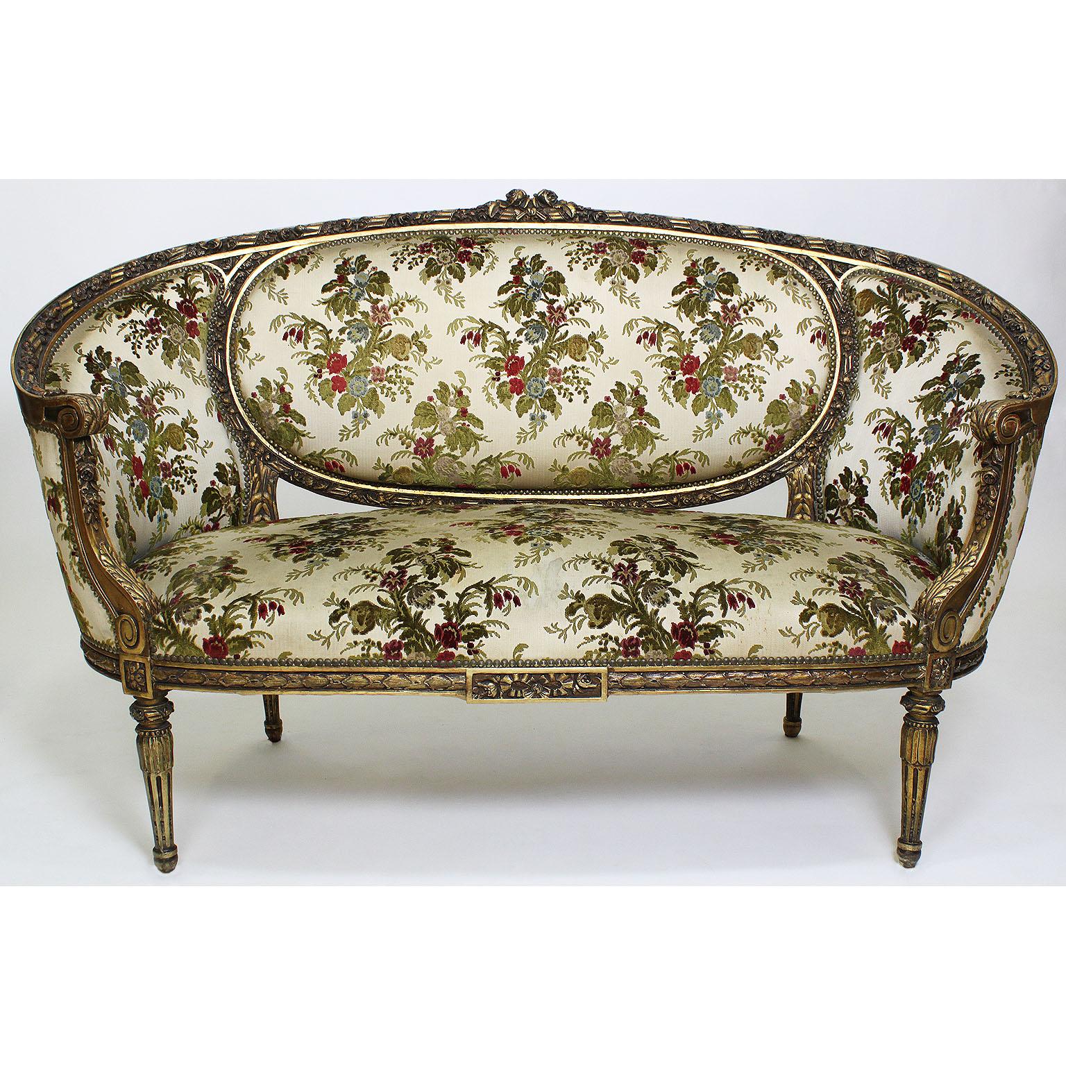 A French 19th-20th century Louis XVI style giltwood carved three-piece salon suite frames. The ornately carved set comprising of a settee and a pair of fauteuils a la Reine (armchairs). The settee with floral carvings and rounded bergère style