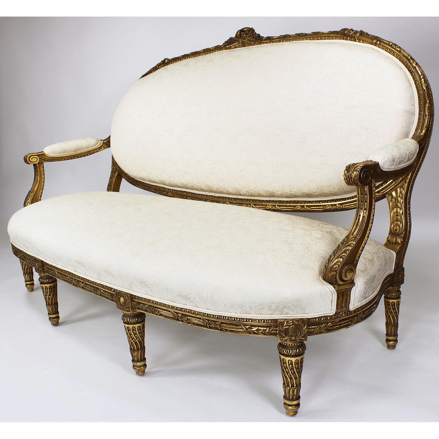 A very fine french 19th-20th century Louis XVI style giltwood carved settee by François Linke (d. 1946). The finely carved frame, upholstered in a recent cream fabric, topped with an allegorical carving of musical instruments within a wreath,