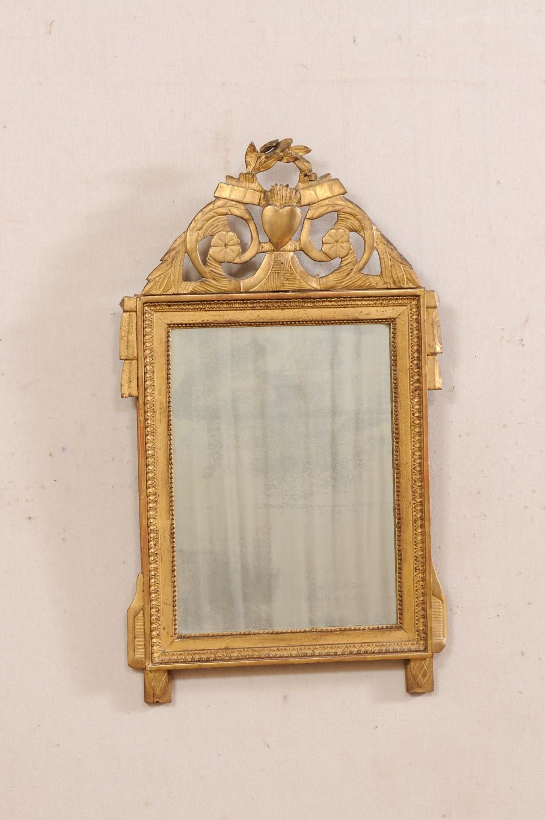 A French carved and gilt wood mirror from the 19th century. This antique mirror from France has a carved wood, rectangular-shaped frame with a lamb's tongue and petite beaded trim accent, and adorn with a pierce-carved raised crest of foliate, a