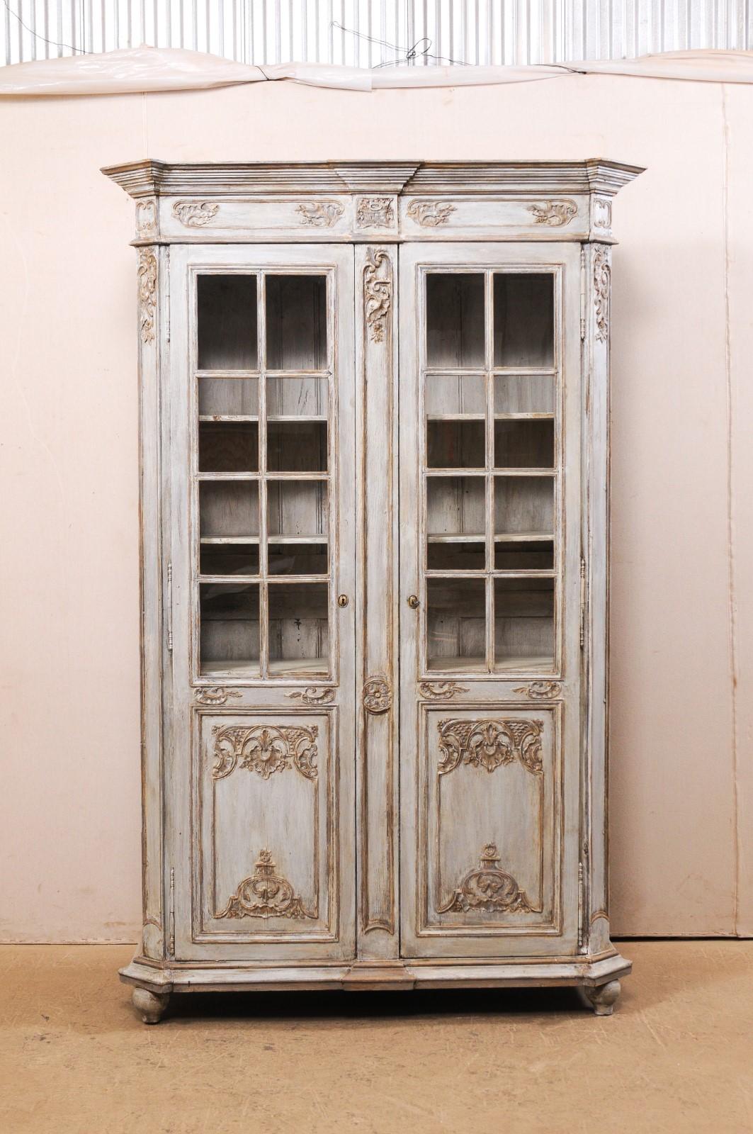 A tall French carved and painted wood cabinet, with glass panels at top, from the 19th century. This antique cabinet from France, which stands approximately 6.75 feet, is fitted with a pair of doors, with upper halves each having 8 glass panels to