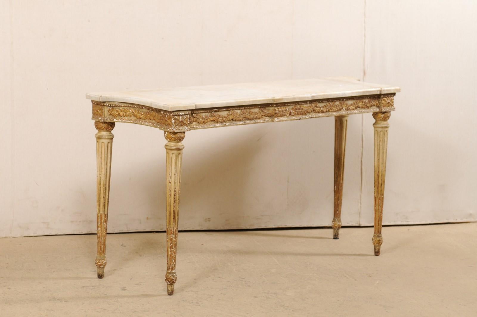 A French carved-wood console table with marble top from the 19th century. This antique table from France features a marble top which rests upon a wood frame with an exquisitely carved apron decorated in a garland of leaves, and flower-heads carved