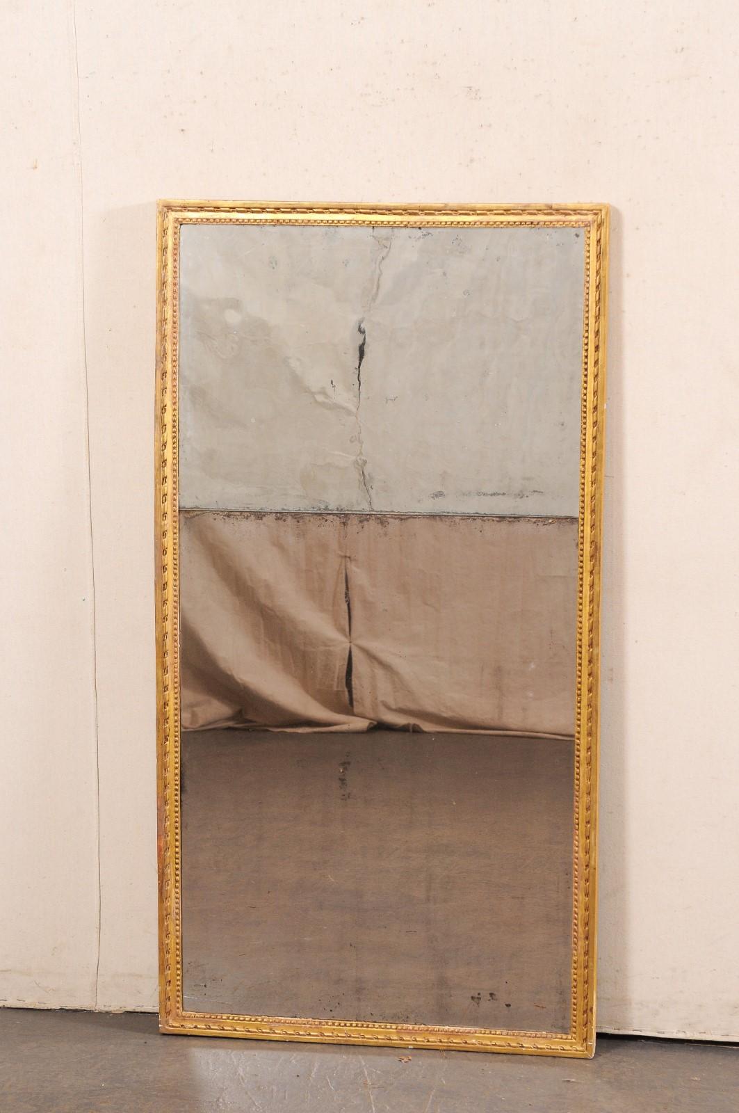 A French carved and gilt wall mirror, with its original glass, from the 19th century. This antique mirror from France has a rectangular-shaped wood frame with cleanly designed outer perimeter, a carved ribbon trim about the frames center, and a