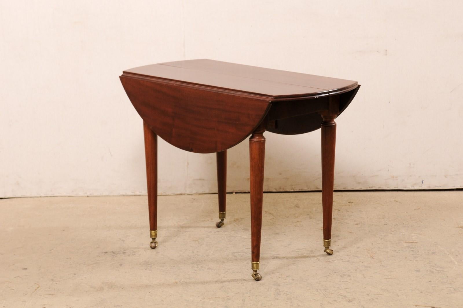 A French mahogany drop-leaf table from the late 19th century. This antique table from France has dual drop-leaf sides that when opened, create an over all round shape. The table is presented upon four round and gently tapering legs, which each