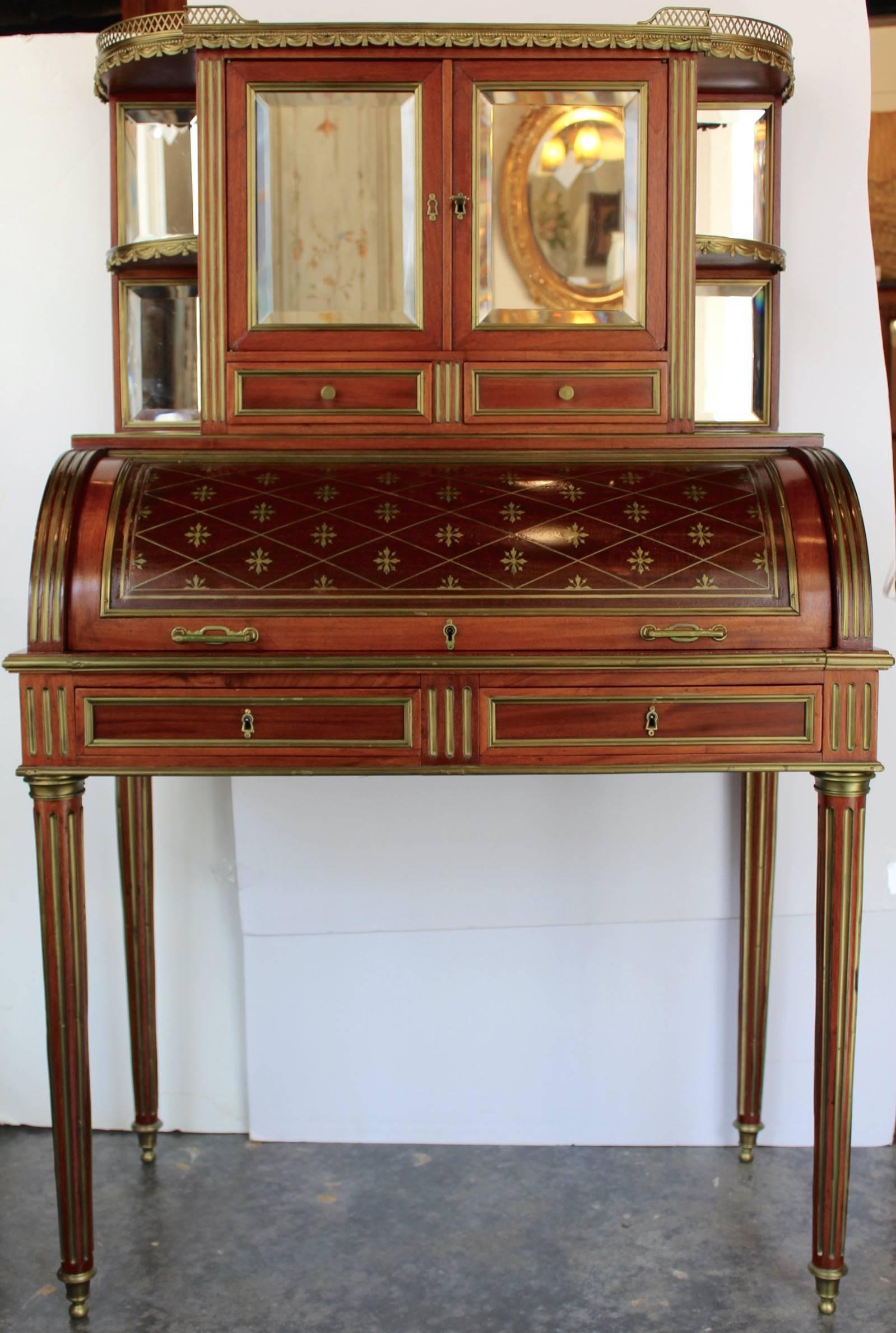 Interesting Louis XVI style mahogany cylinder desk with a white marble top having a brass gallery rail and under which a cabinet with two mirrored glass doors, four quarter round mirrored shelves and two short drawers. All glasses are beveled.
This