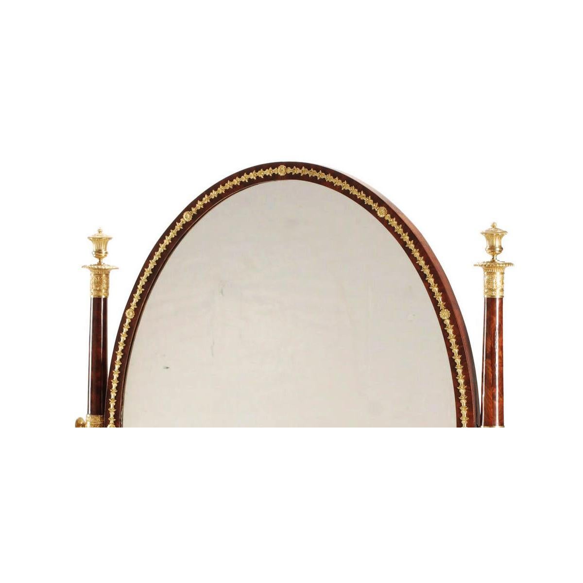 Très beau miroir pivotant de style Napoléon III Empire du XIXe siècle, en acajou et bronze doré, monté sur pied. La plaque de miroir à encadrement ovale est surmontée de couronnes de laurier en bronze doré de style Empire, flanquée de supports