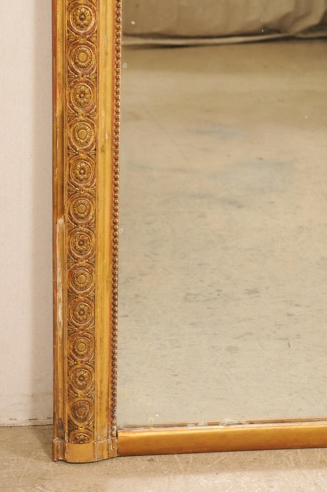 A large French carved and gilt wood mirror from the late 19th century. This antique mirror from France features a rectangular-shaped surround with a repeating floral in medallion motive carved within the center molding, and sweet petite beaded inner