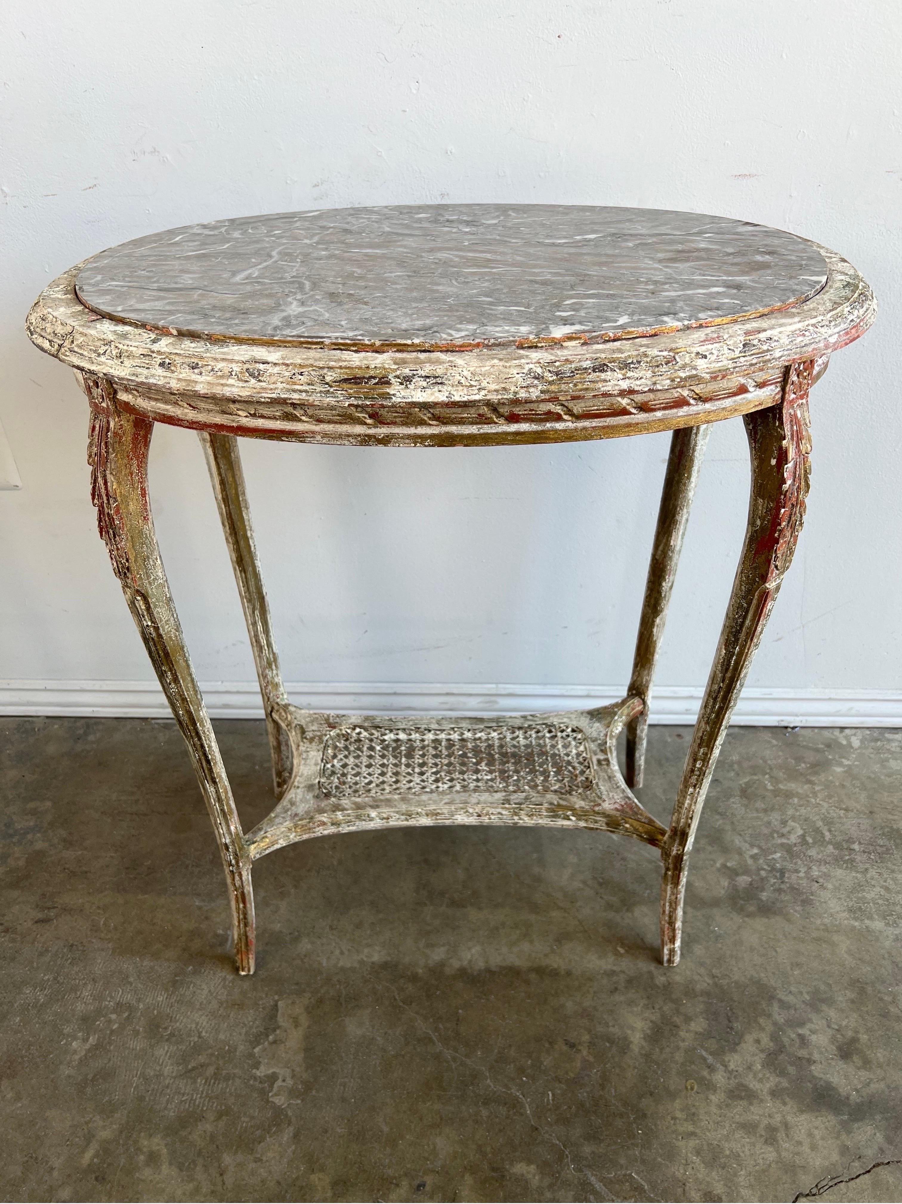 19th Century French oval carved wood & cane side table. The table stands on four elegant cabriole legs that meet at a bottom cane shelf. Great worn painted finish with bits of gold leaf seen throughout. Grayish taupe oval shaped marble inset top.