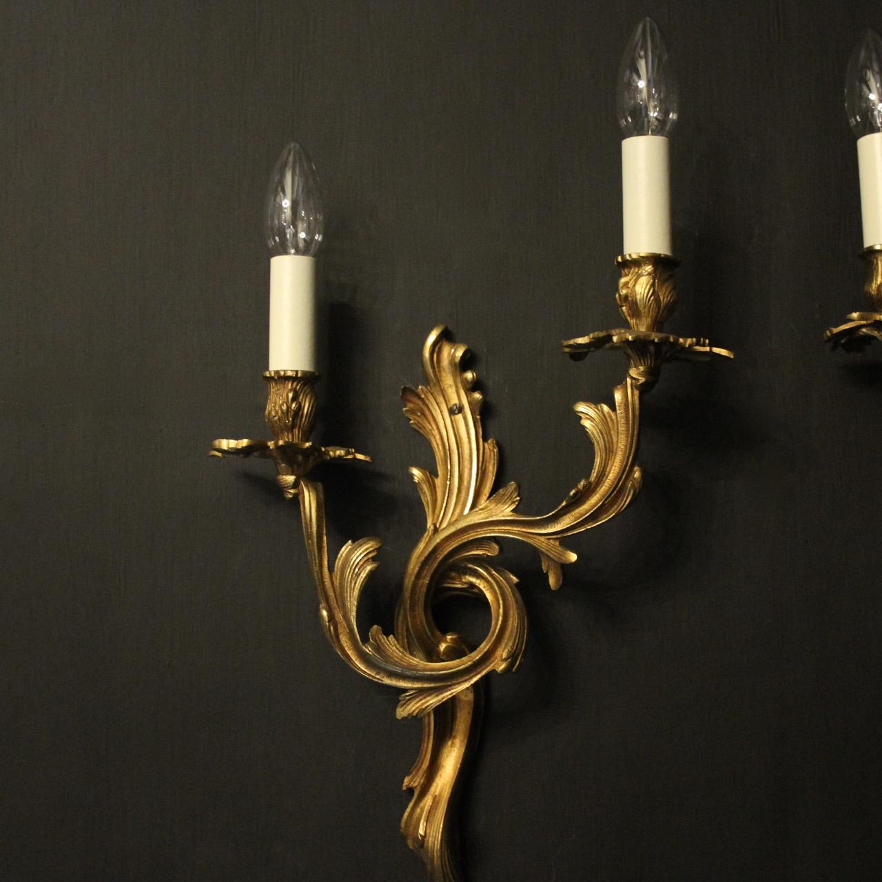 A French pair of gilded bronze twin arm opposing antique wall sconces, the leaf scrolling arms with leaf bobeche drip pans and bulbous candle sconces, issuing from a decoratively cast opposing leaf backplate, good original color and nice crisp