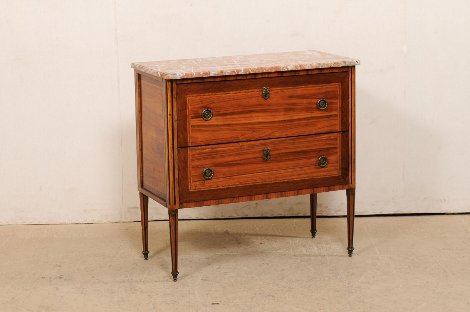 A French raised commode with marble top and inlays from the 19th century. This antique chest from France has a marble top with ogee-edging and rounded at front corners, atop a case which houses two deep-set, dove-tailed drawers, and raised upon