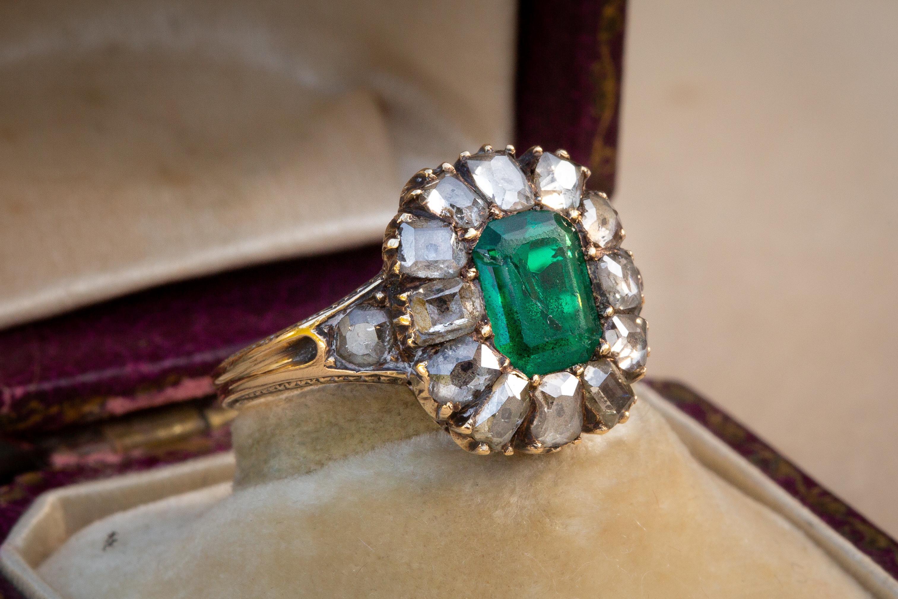 This spectacular antique French gold cluster ring dates to the second half of the 19th century. In the centre rests a step-cut natural emerald with a fantastic hue and saturation. It weighs approximately 1.2Ct and is likely to be of Columbian